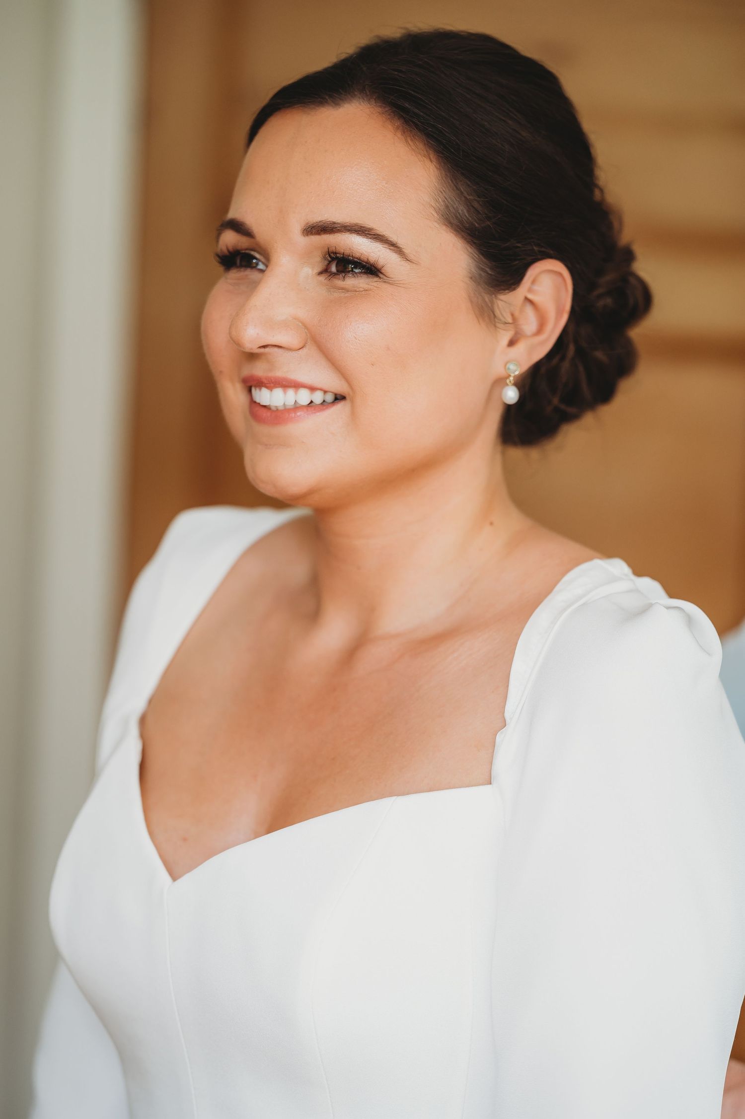 Beautiful bride in white dress with elegant dark updo hairstyle smiles radiantly on her wedding day.