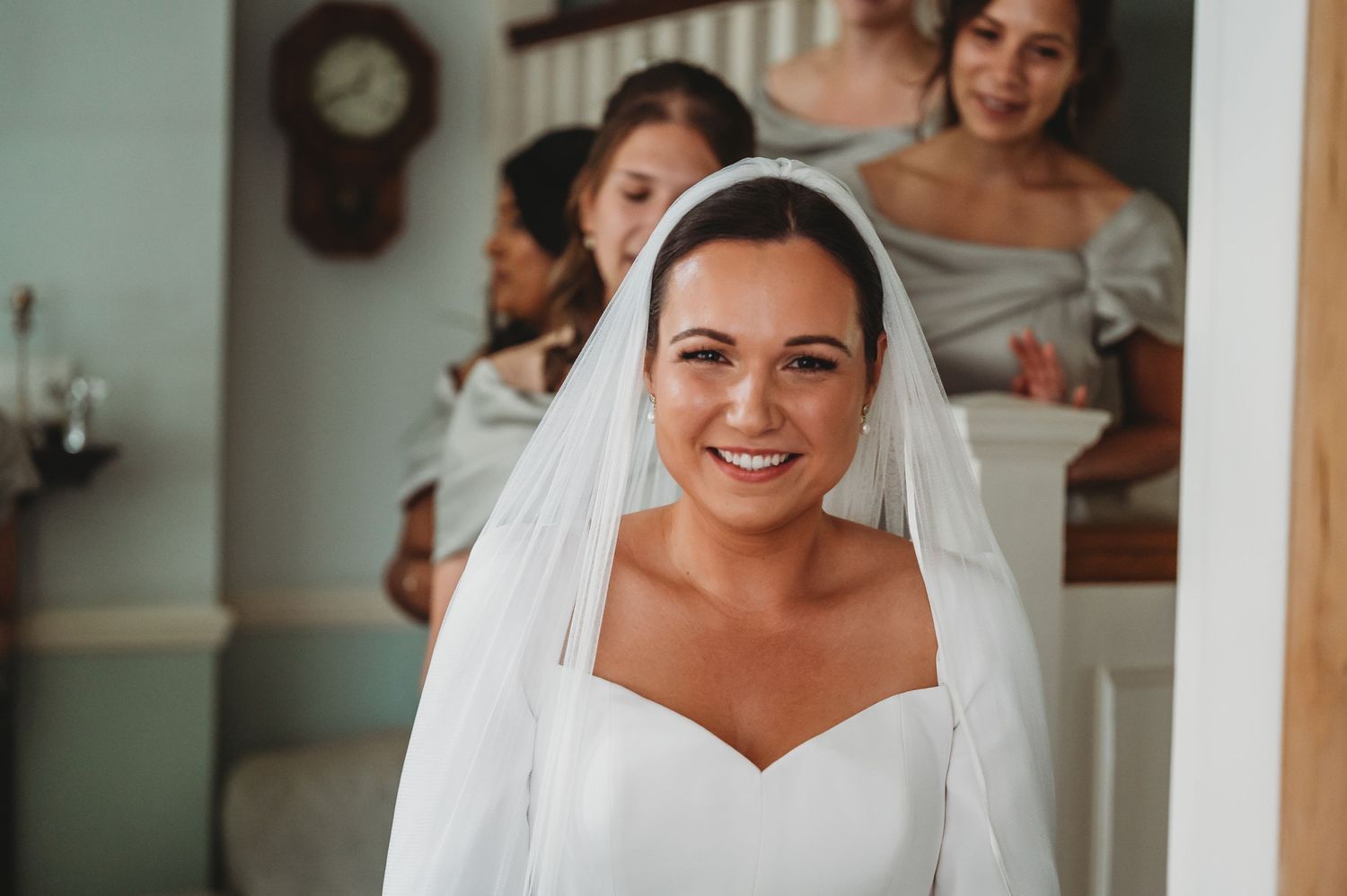 A radiant bride wearing a white wedding gown and veil smiles joyfully during wedding preparations.