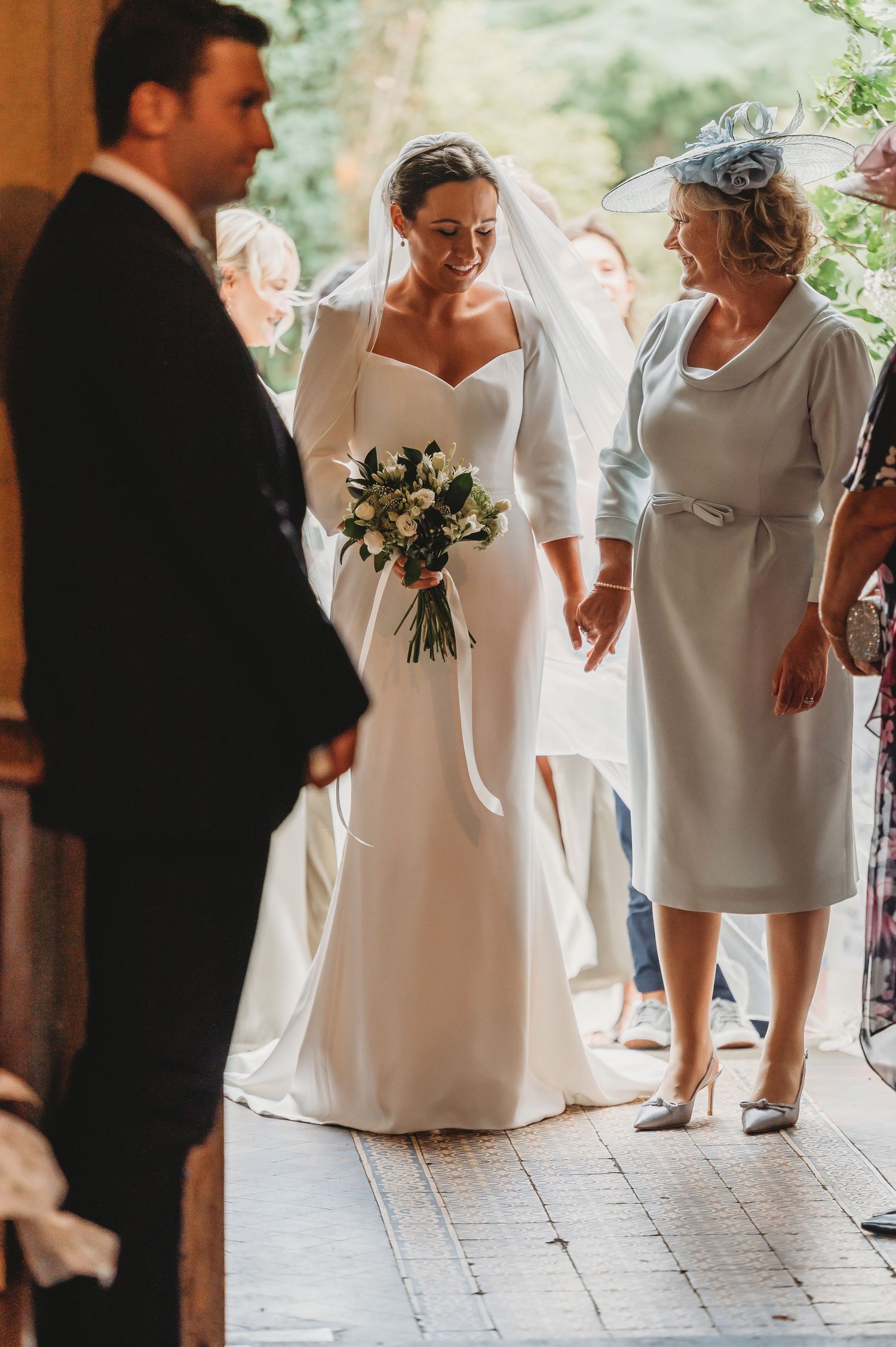 A tender wedding moment captured as the bride holds a bouquet surrounded by family.