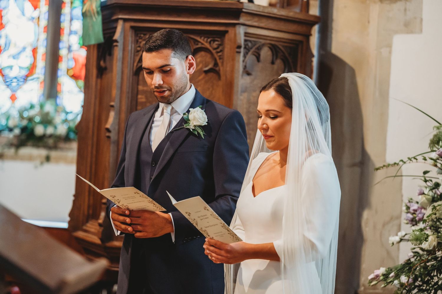 A couple reads from hymn books during their wedding ceremony in a traditional church setting.