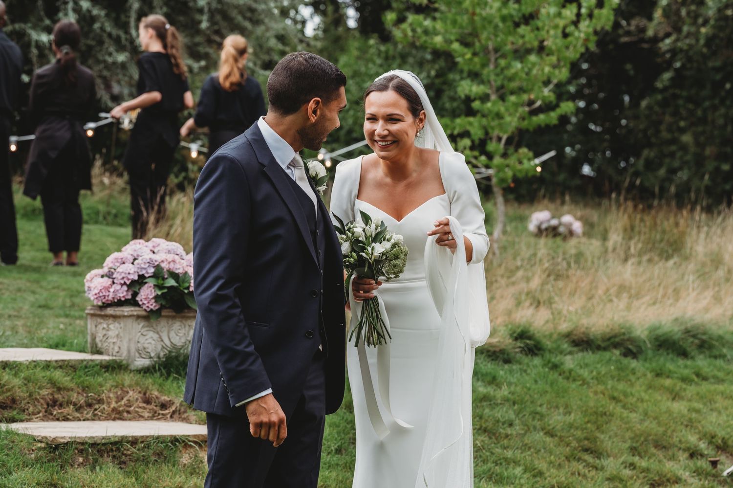 A couple shares a joyful moment during their outdoor wedding ceremony in a garden setting with natural greenery.