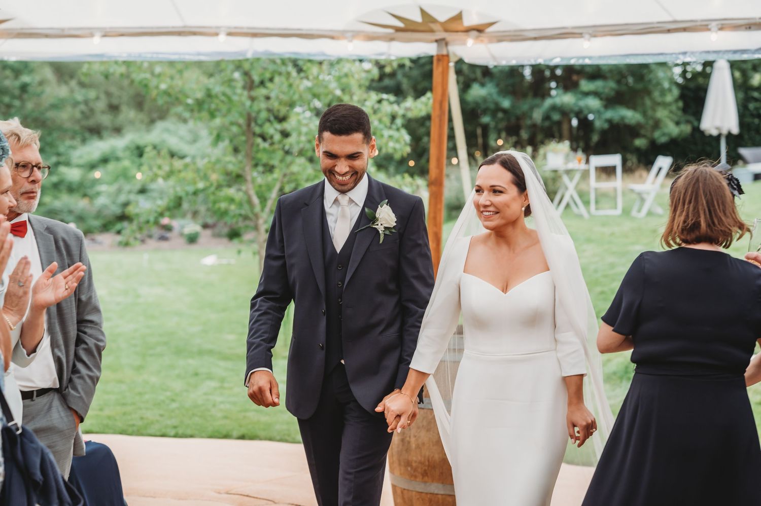 A couple celebrates during their outdoor garden wedding ceremony, holding hands and smiling while walking down the aisle.