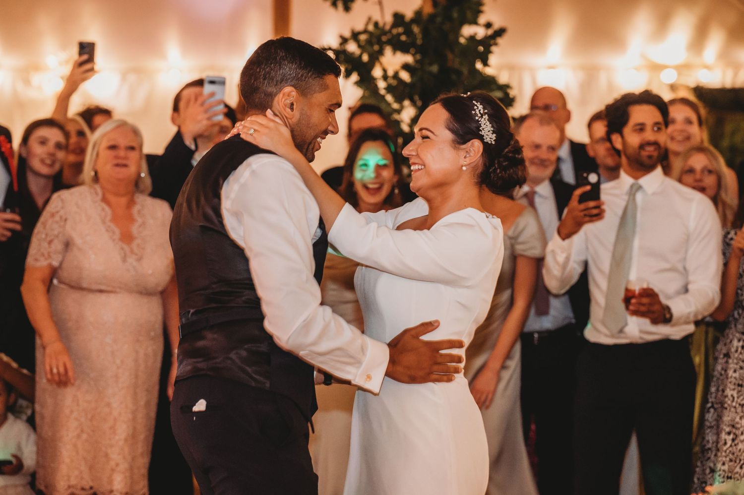 Happy couple shares a romantic first dance at their wedding reception while guests watch and celebrate in the background.