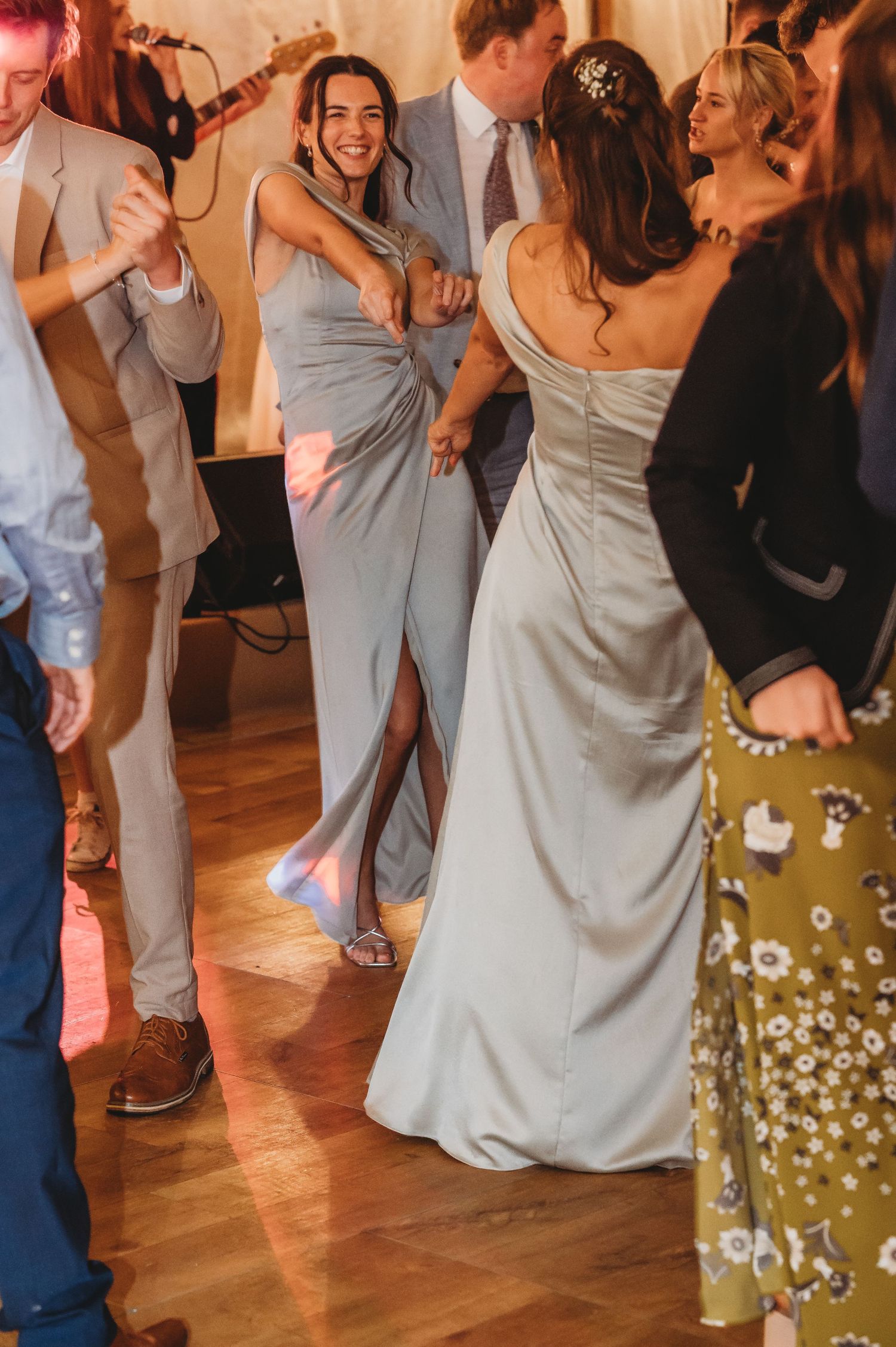 Wedding guests in gray formal attire dance and celebrate on a wooden dance floor at a reception.
