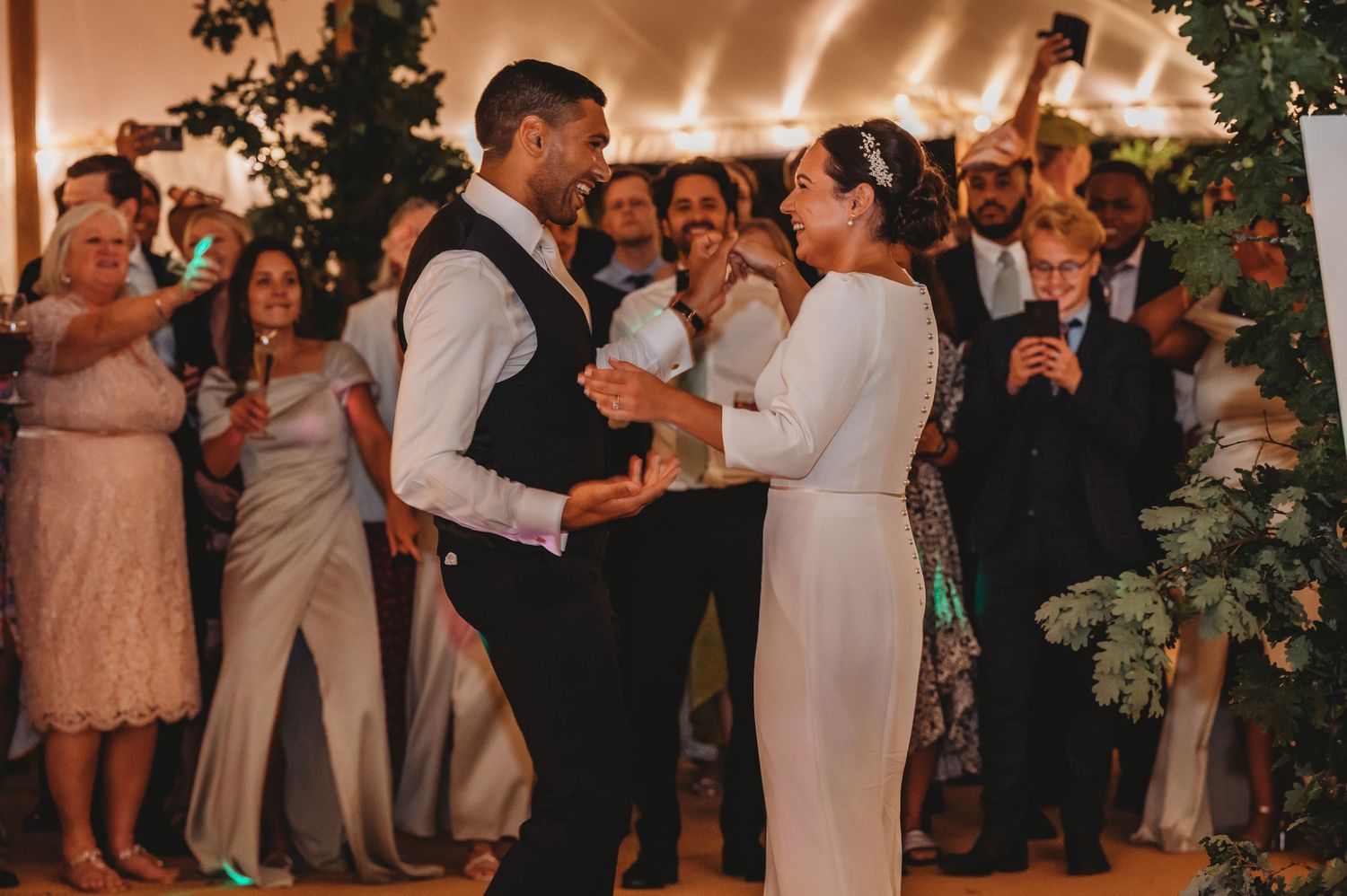 A couple sharing their first dance at a wedding reception with guests watching in a warmly lit venue.