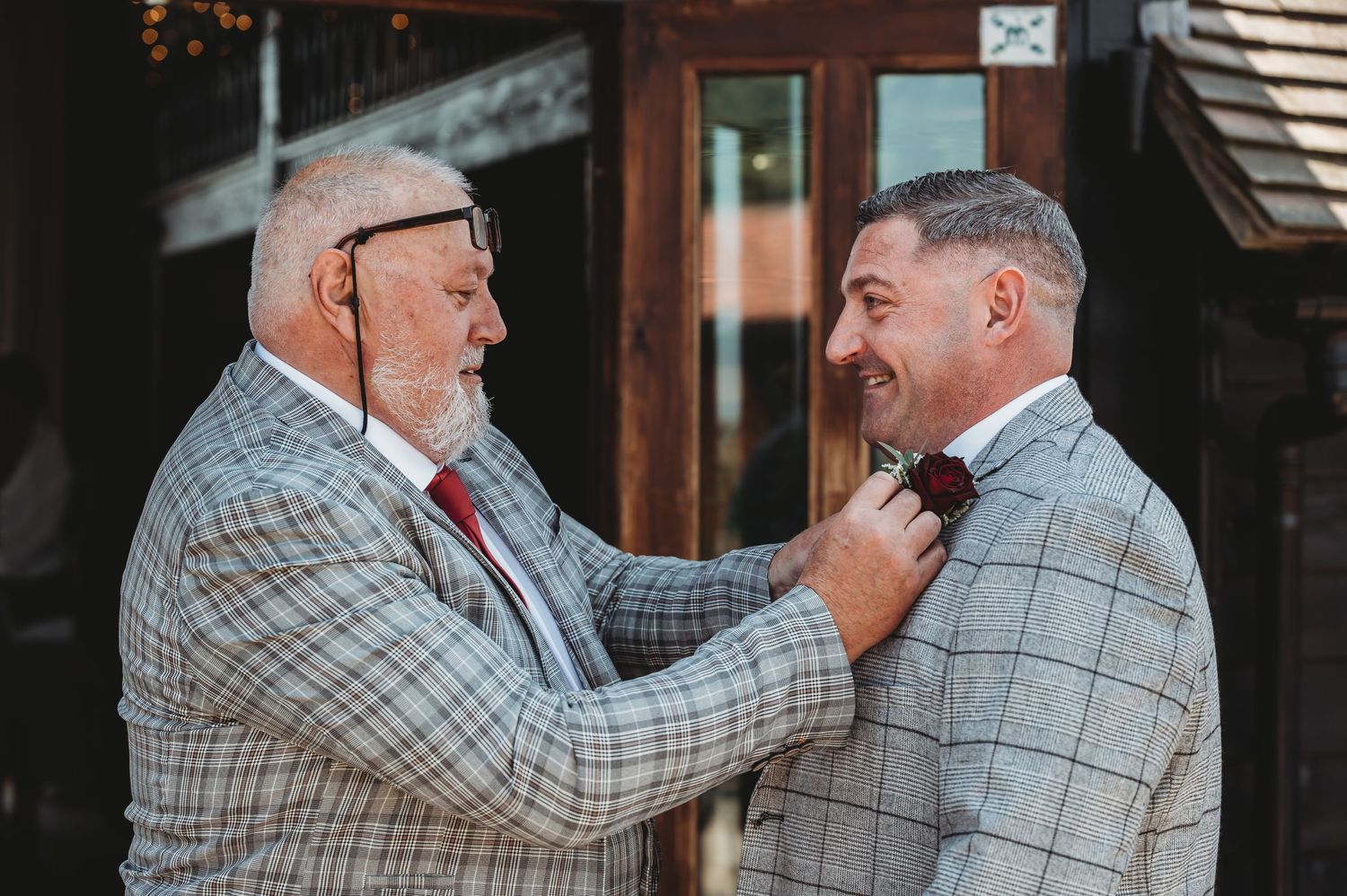 Two people share a touching moment in matching plaid suits while adjusting each other's ties.