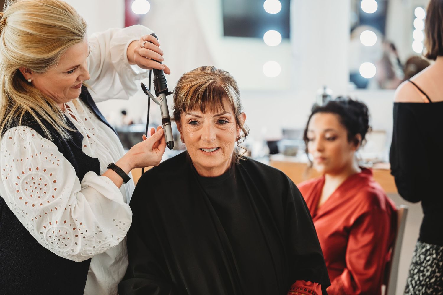 A stylist works on a client's hair in a bright salon setting.