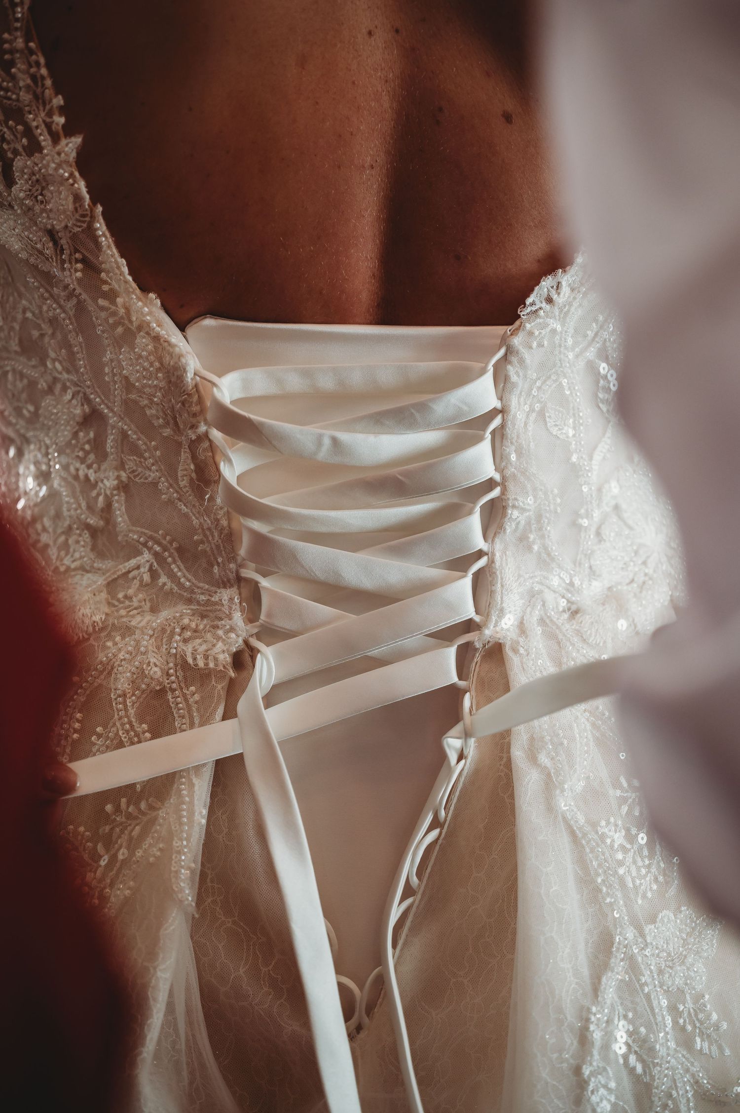 Close-up detail of a white lace wedding dress corset with satin ribbon lacing up the back.