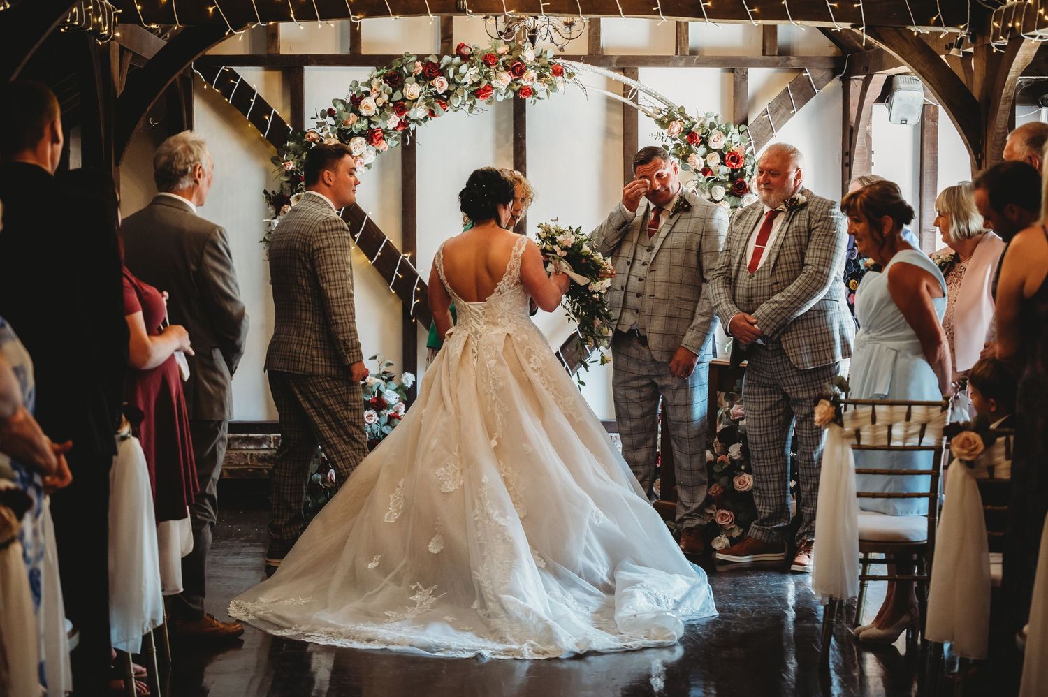 Indoor wedding ceremony with bride in sparkly ballgown dress standing at altar with wedding party in gray suits.