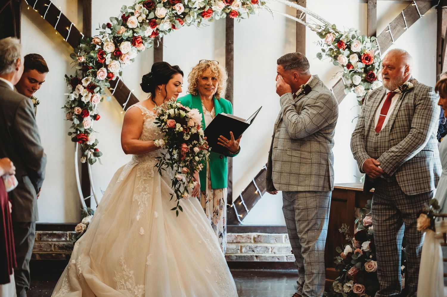A heartfelt wedding ceremony takes place under a floral arch as attendees share an emotional moment during the vows.
