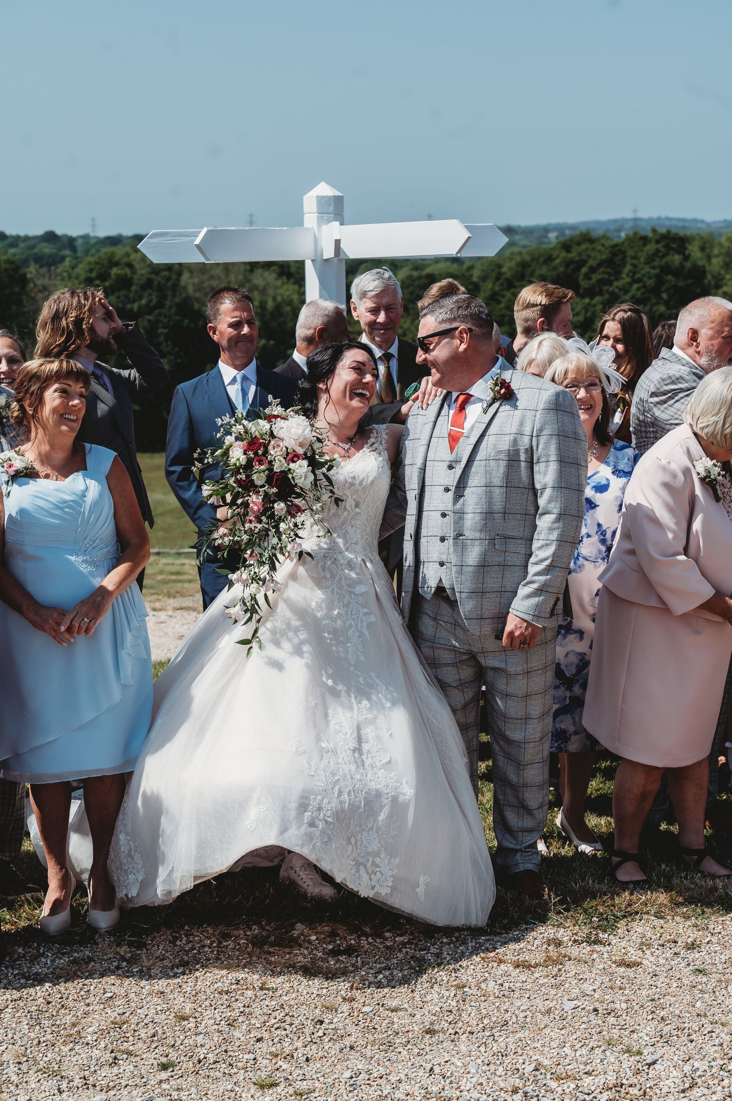 A joyous outdoor wedding celebration on a sunny day with guests gathered around a couple in traditional wedding attire.