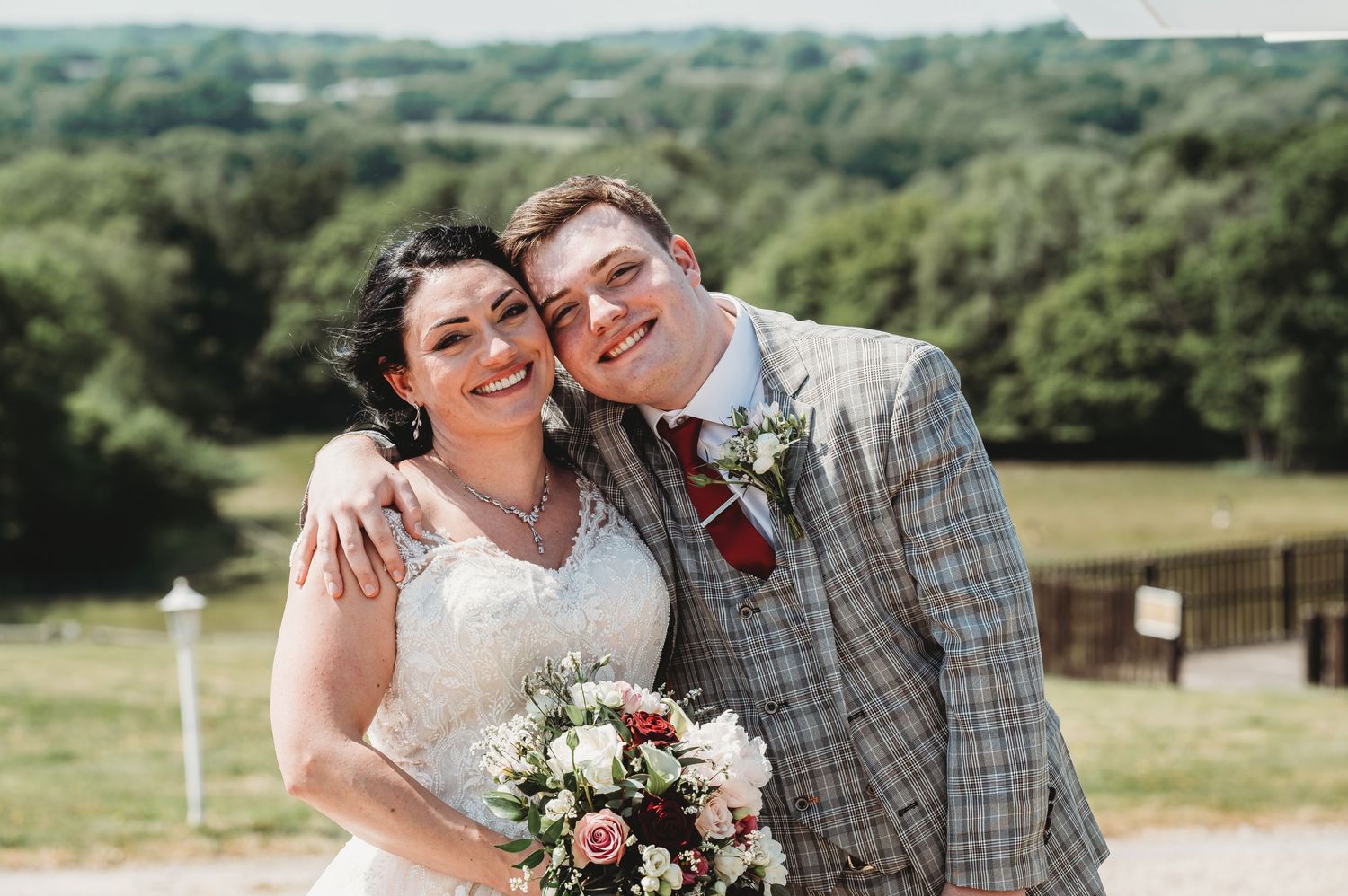 A happy couple celebrates their countryside wedding on a sunny day, with rolling hills and greenery in the background.