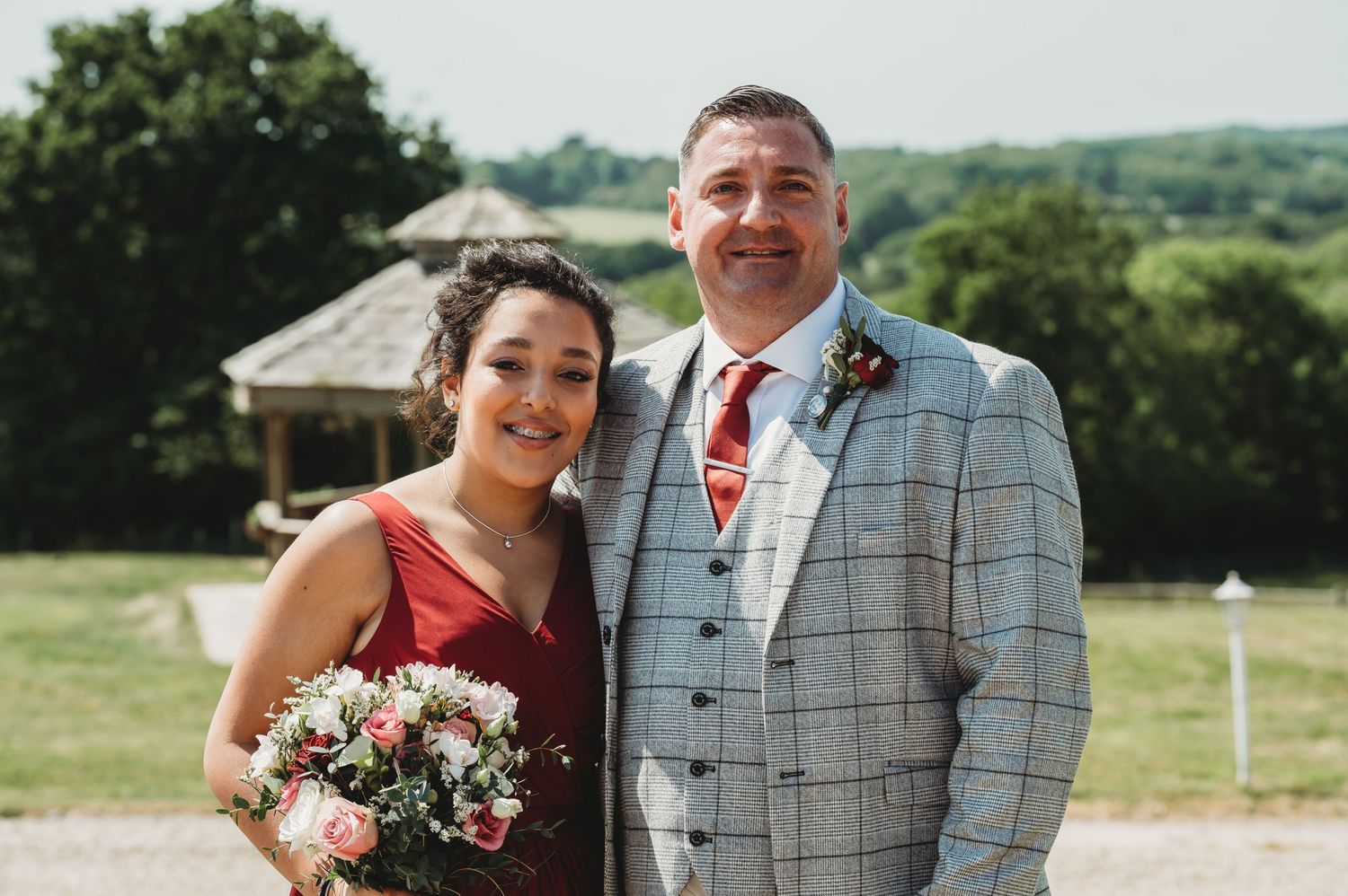 A couple poses together outdoors at a scenic countryside wedding venue with rolling hills in the background.