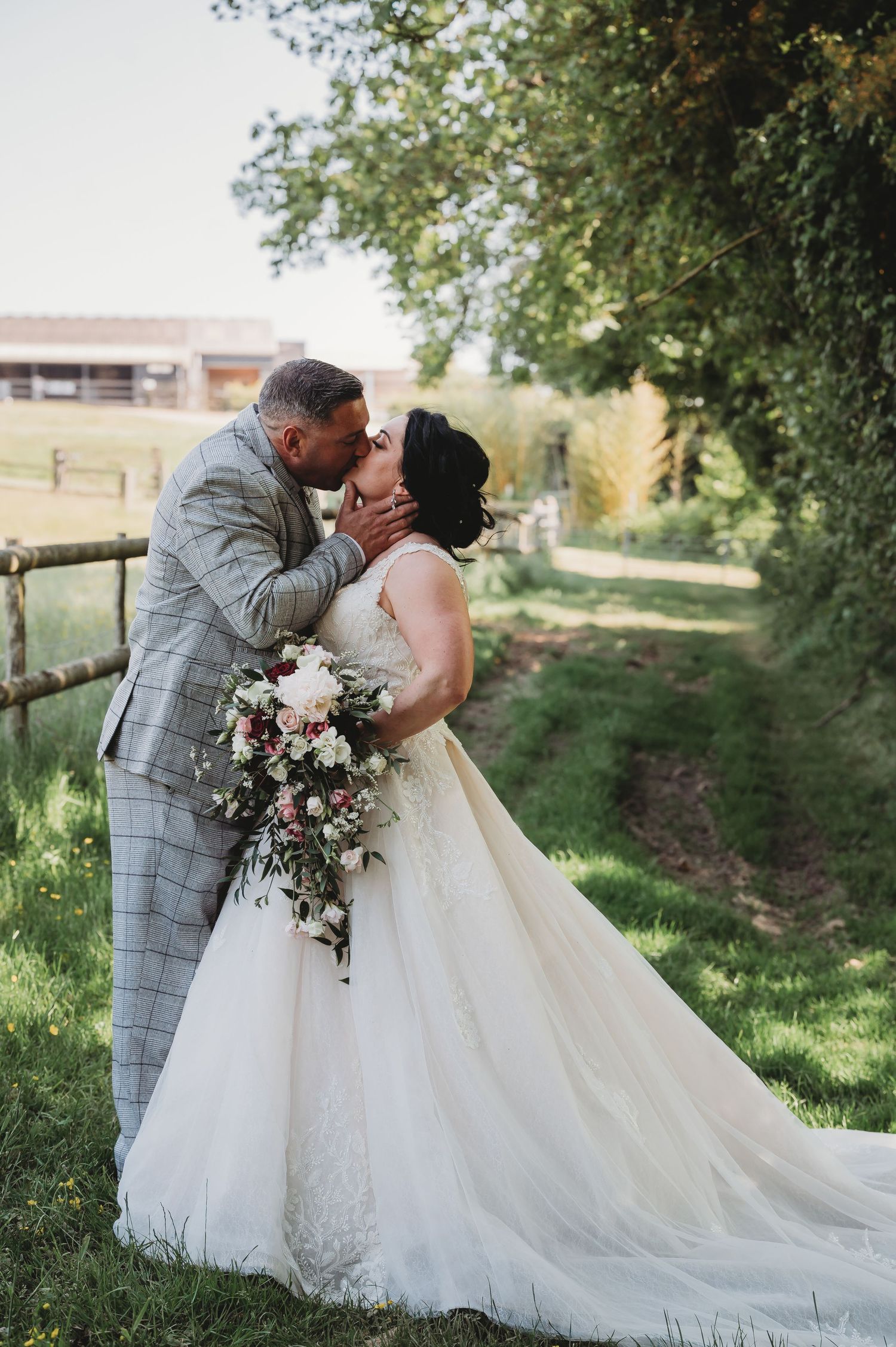 Intimate wedding moment captured on a countryside path with the bride in white holding a pink and white bouquet.
