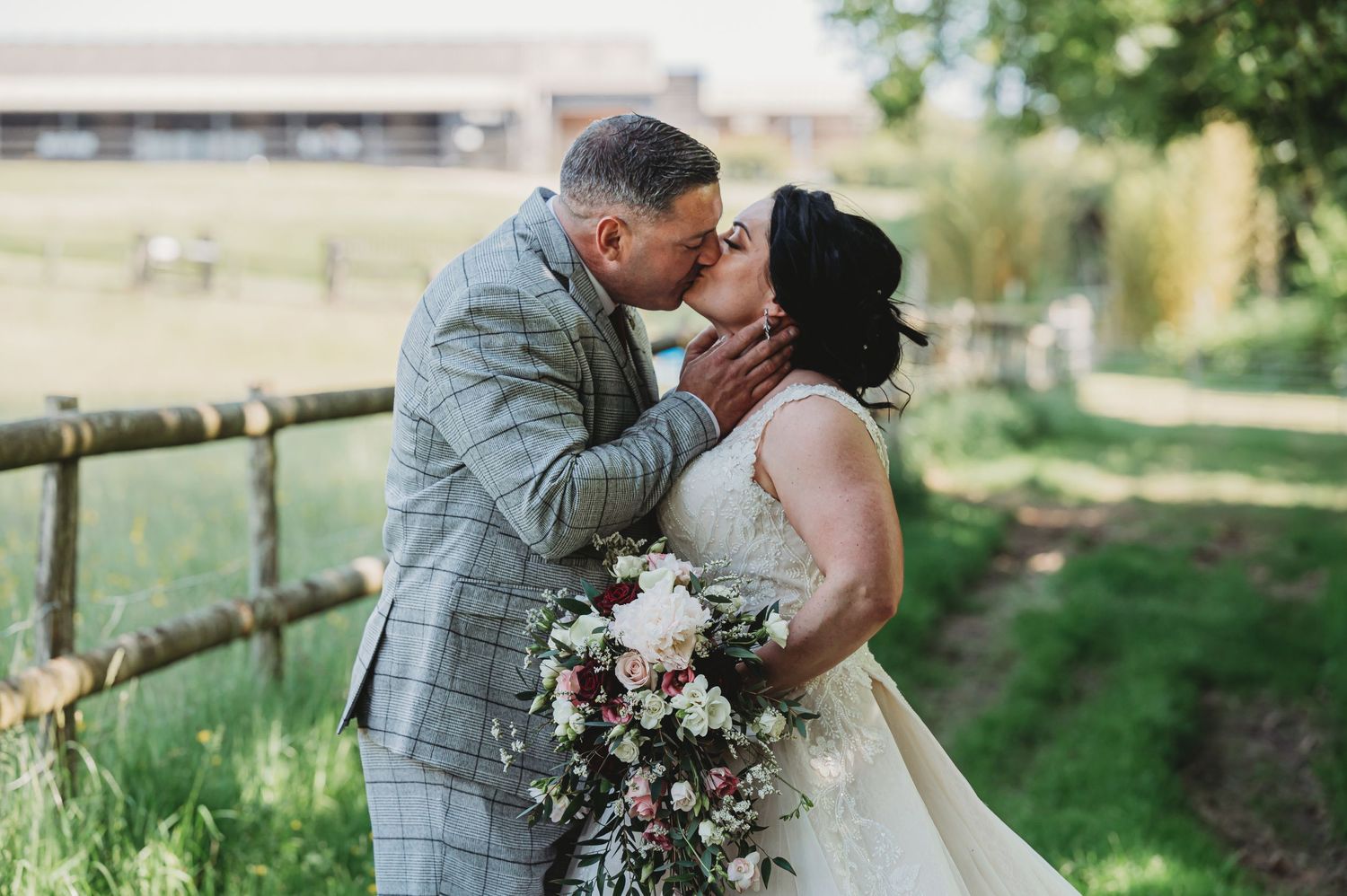 A couple shares romantic kiss during wedding photoshoot in countryside setting.