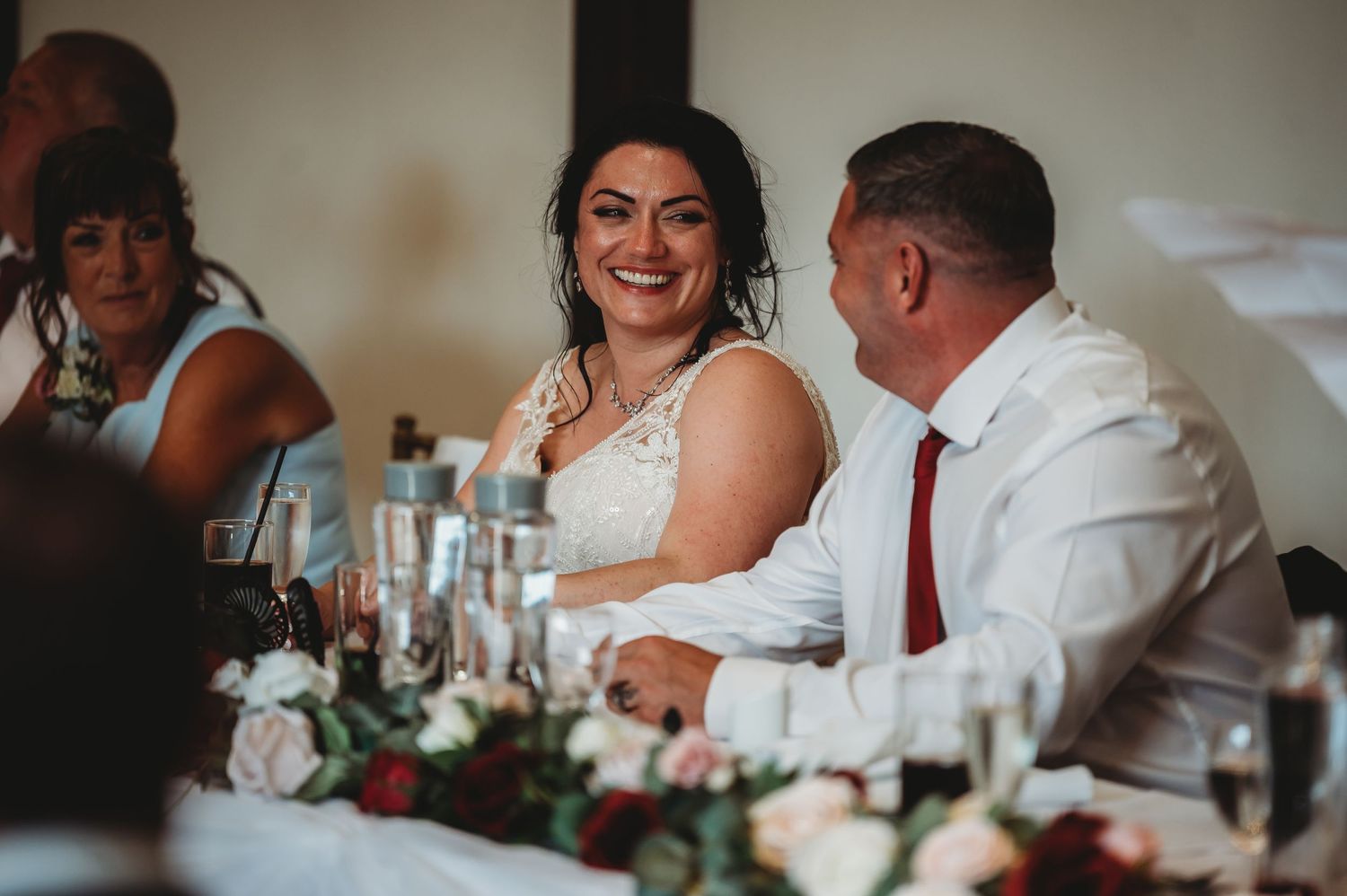 Bride and guests share a joyful moment at wedding reception table decorated with floral centerpieces.