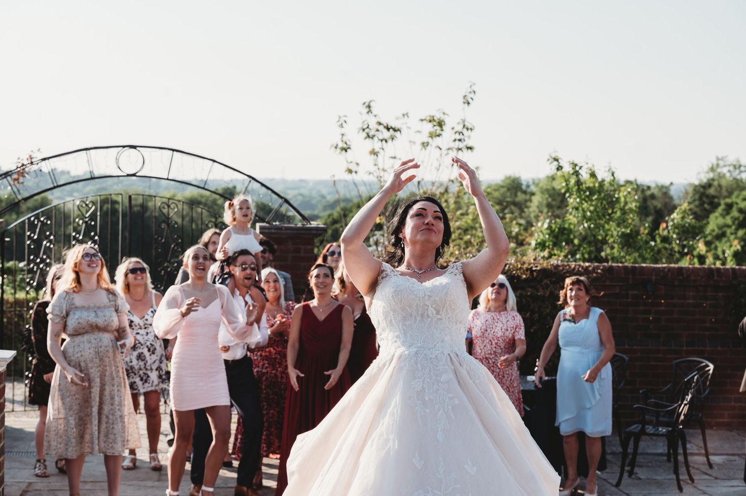 A bride in a white wedding dress throws her bouquet during the traditional bouquet toss at an outdoor wedding reception.