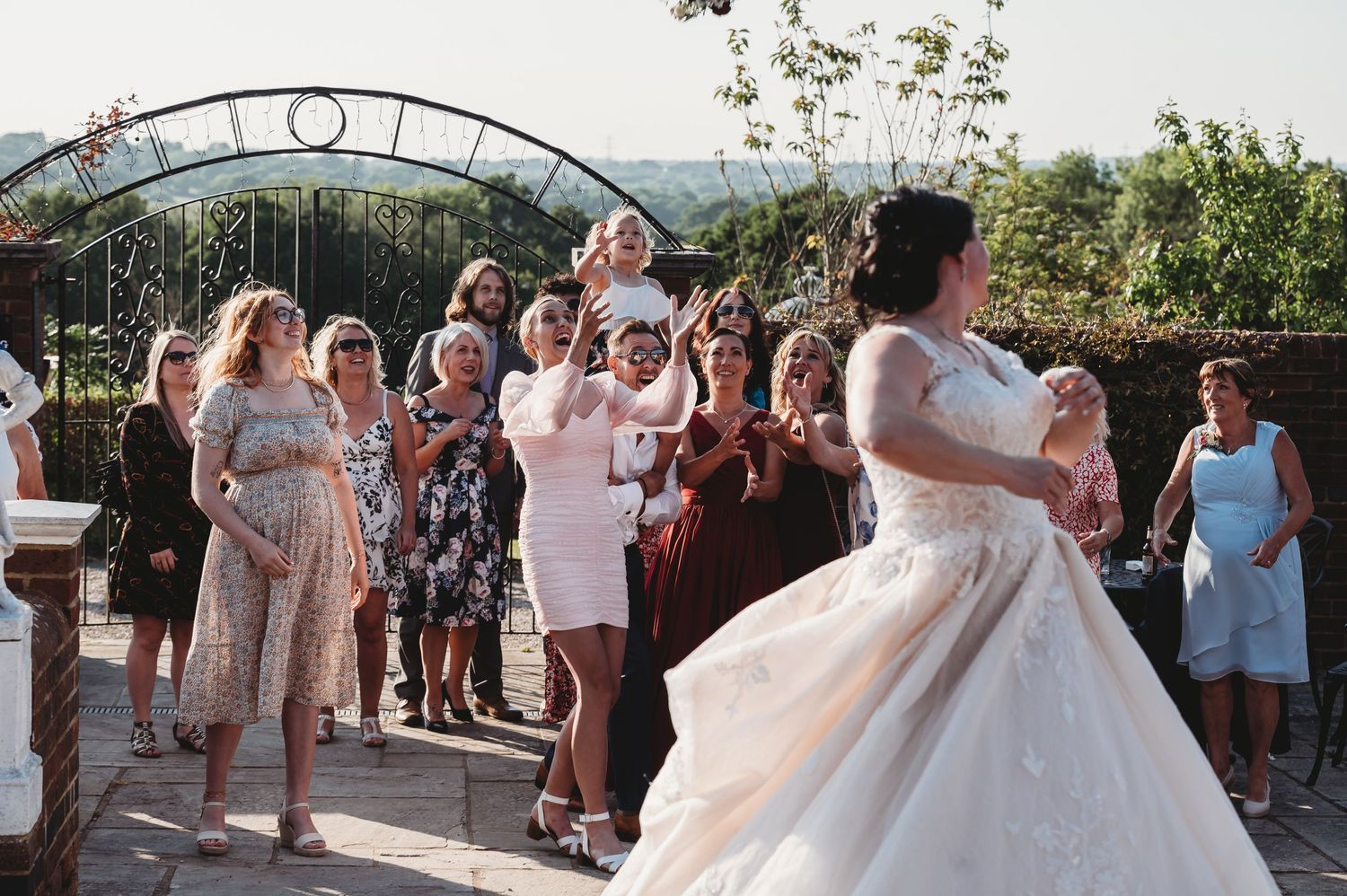 Wedding guests gather to watch a first dance celebration at an outdoor venue under a decorative arch at sunset.