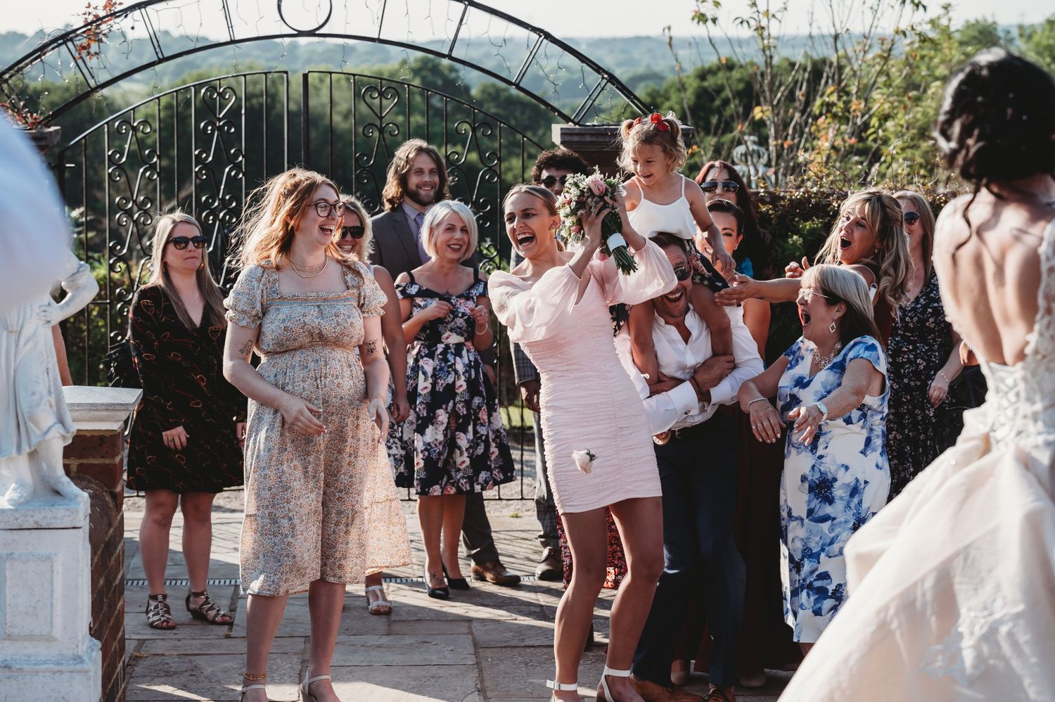 Wedding guests celebrate on an outdoor patio under an arched trellis during a sunny afternoon gathering.