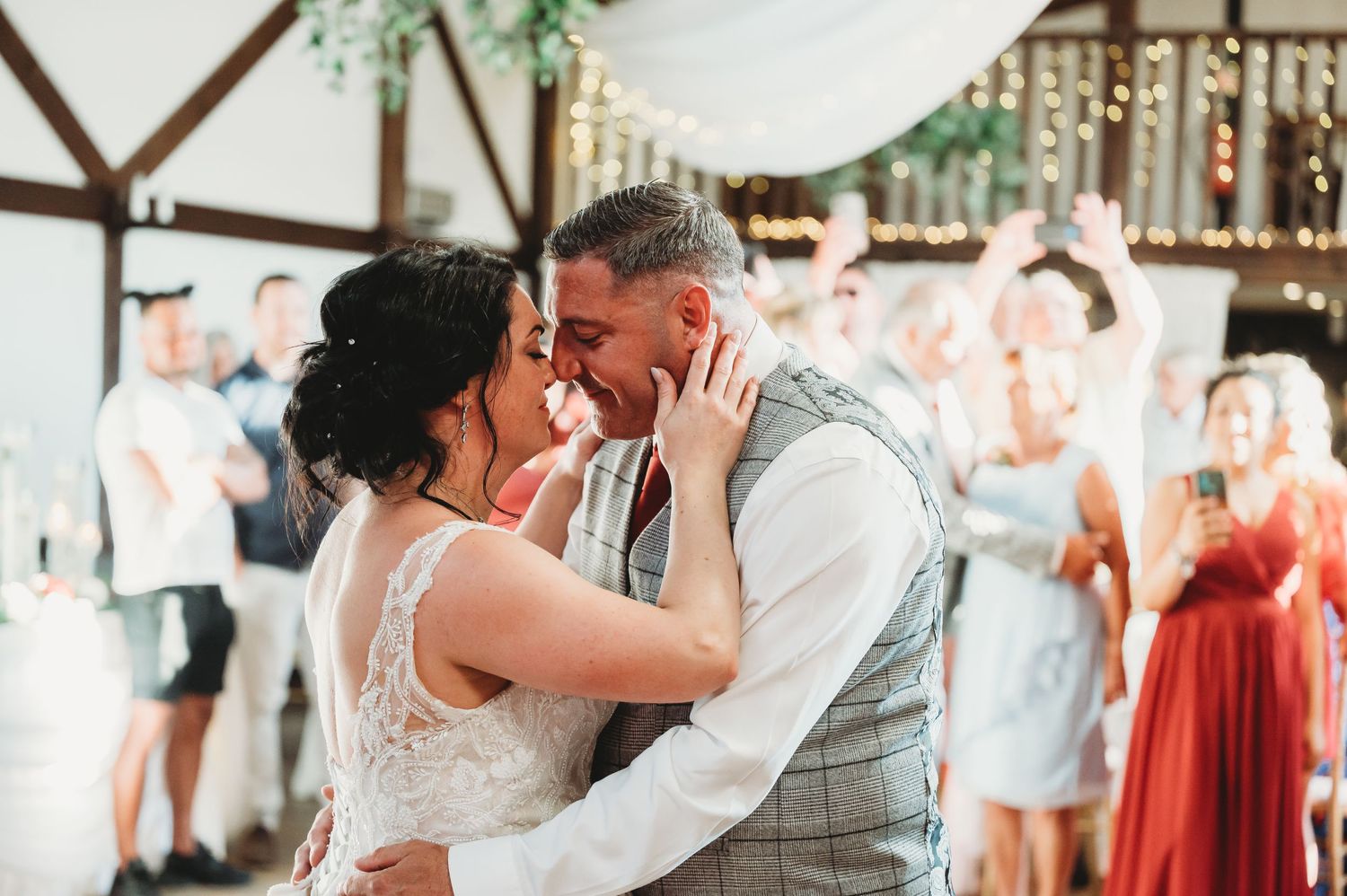 A romantic first dance moment between newlyweds at a rustic barn wedding reception with guests watching in the background.