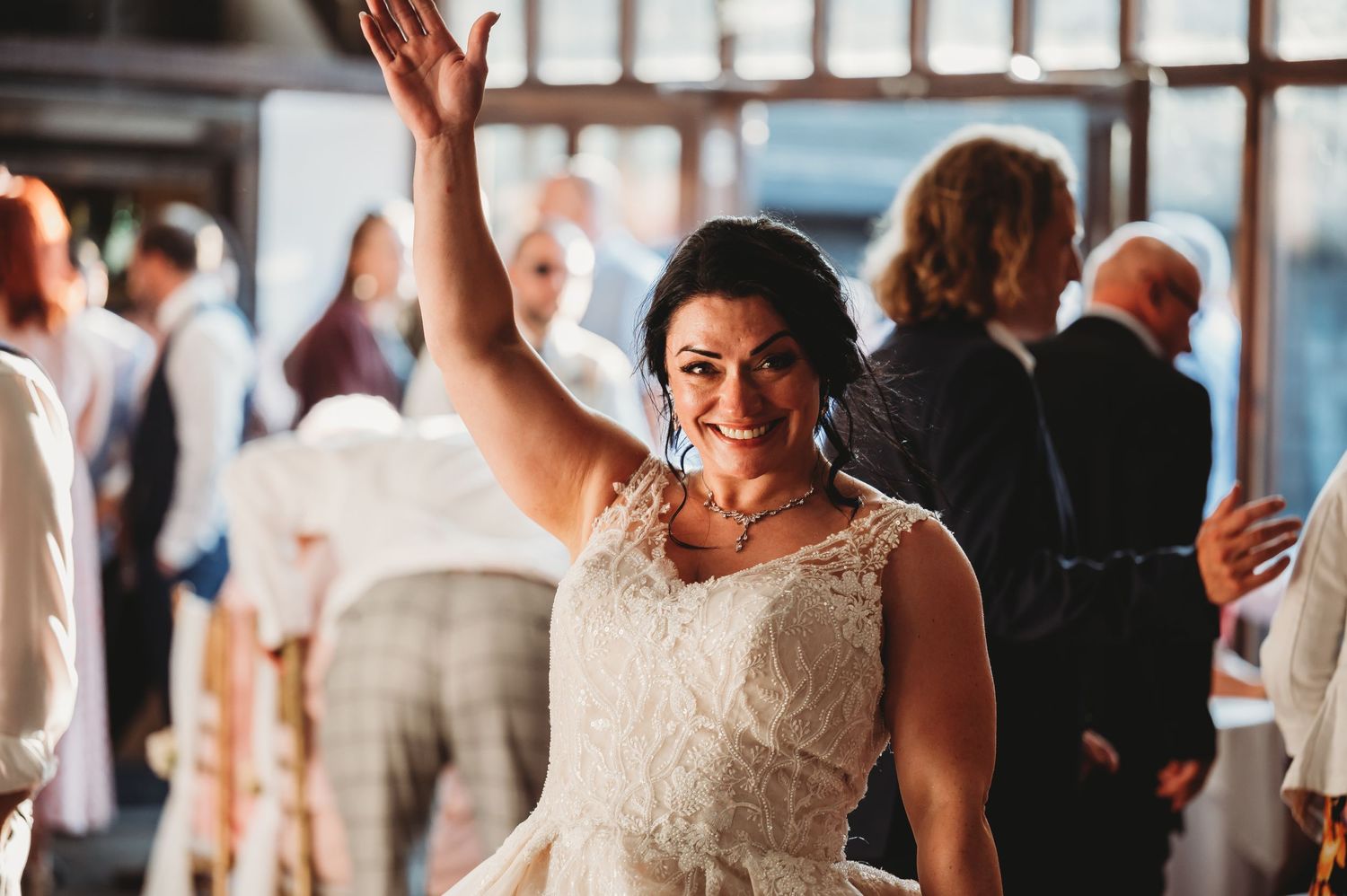 A bride in an elegant lace wedding dress dances with her arm raised during a wedding reception celebration.