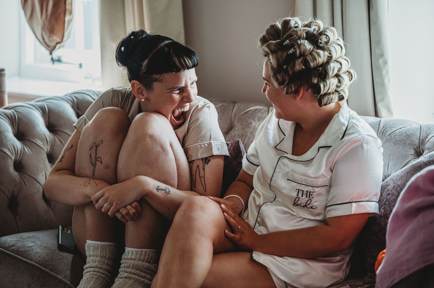 Two people in casual attire share a relaxed conversation on a gray couch.
