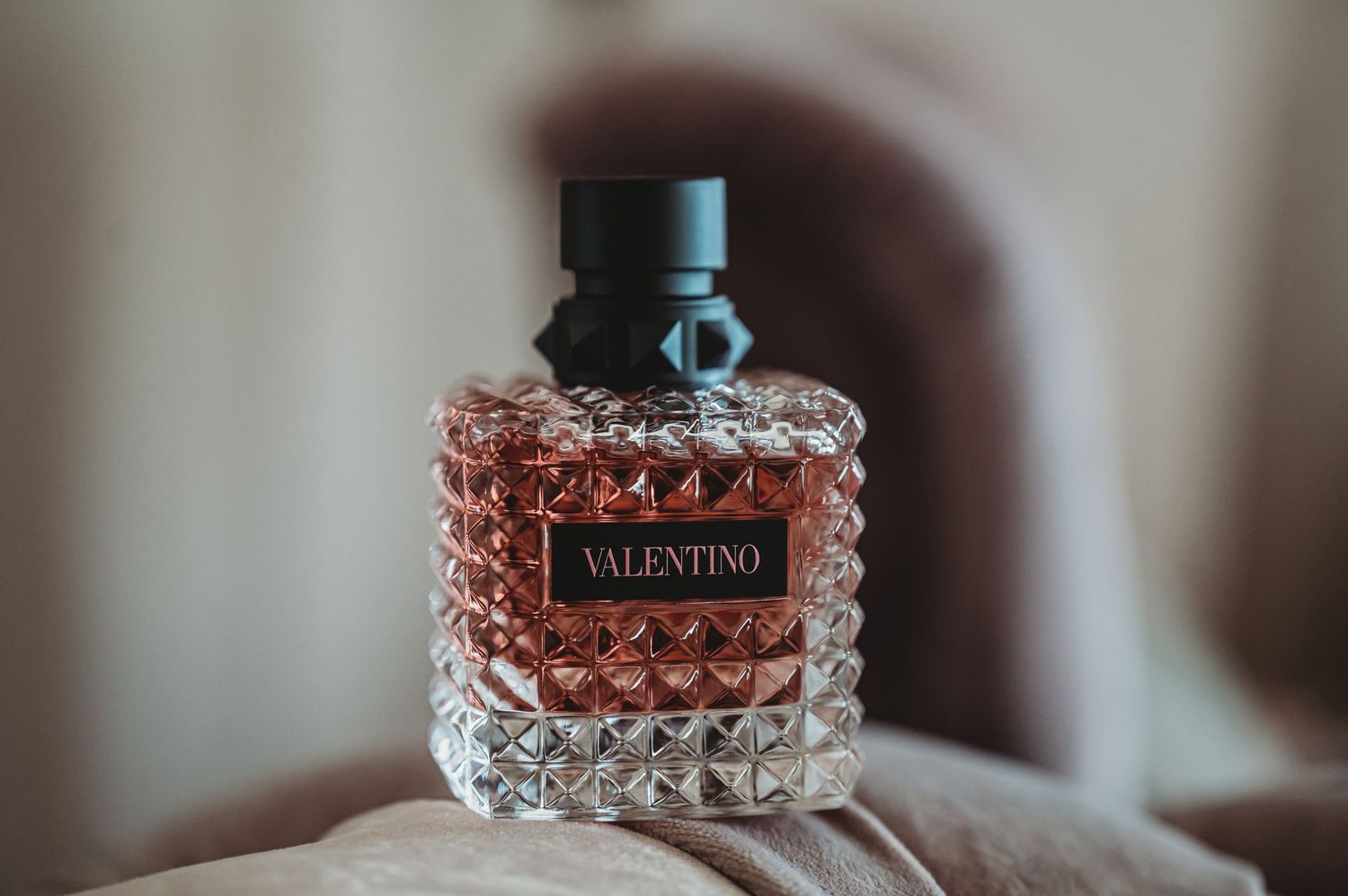 Crystal bottle of Valentino perfume photographed in soft moody lighting.