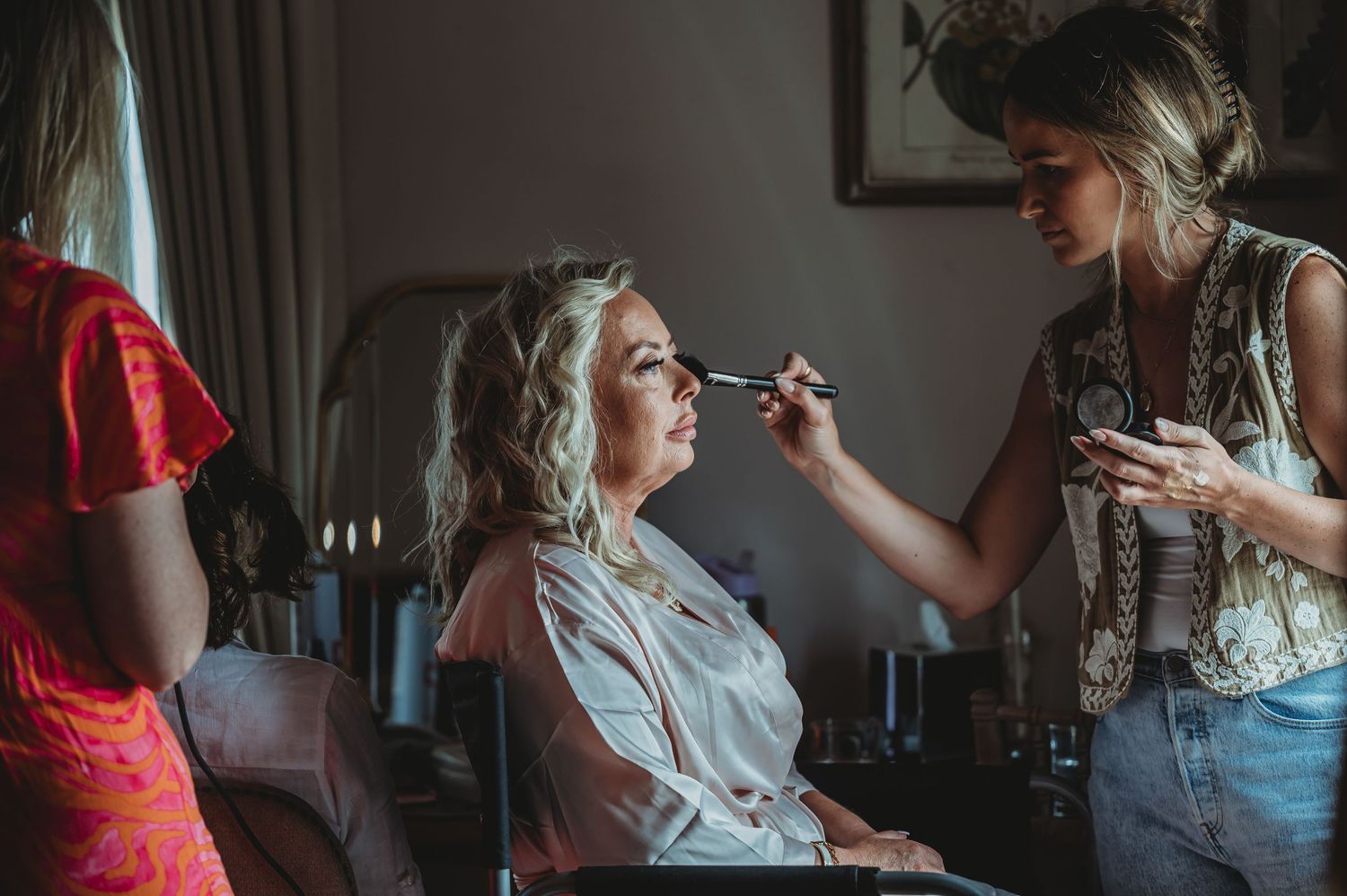 Getting ready moment showing wedding day makeup application in a softly lit room with vintage ambiance.
