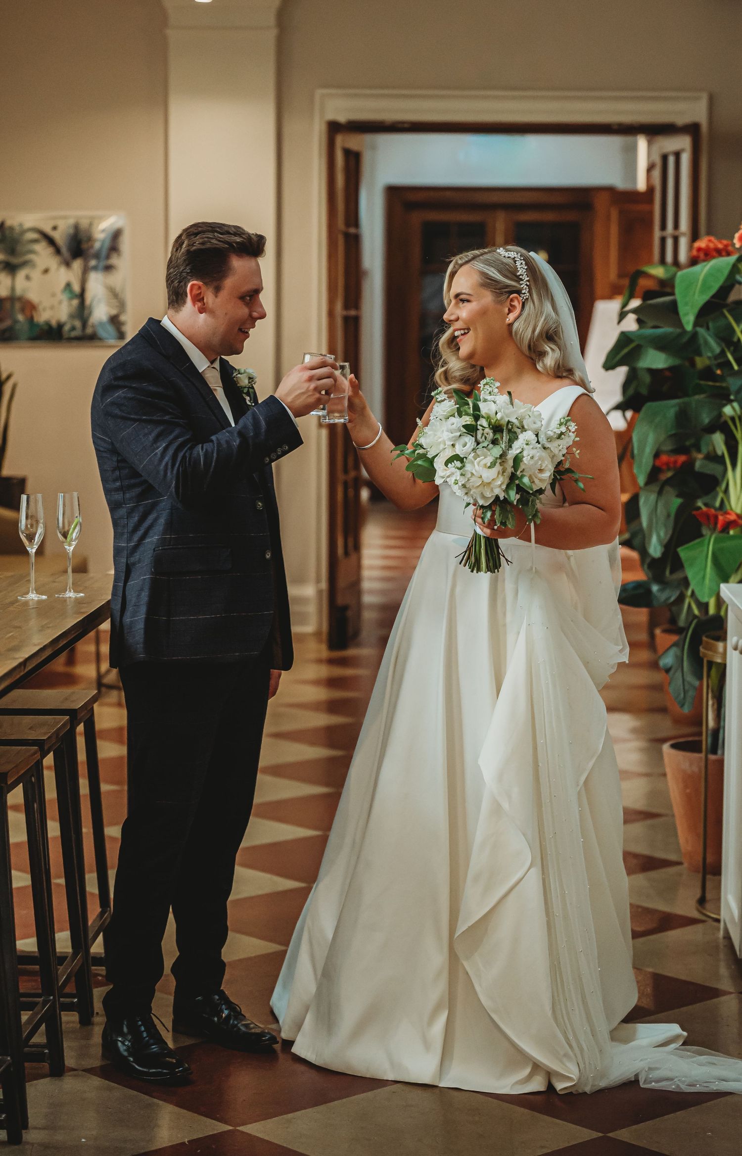 A joyful moment between a newlywed couple sharing a candid dance in an elegantly decorated room with champagne flutes nearby.
