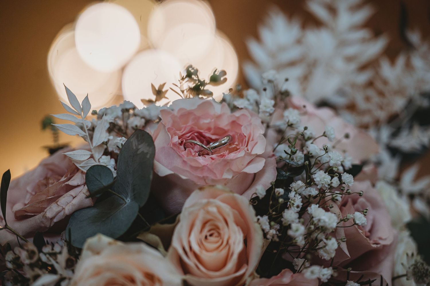 Soft pink and cream roses with eucalyptus leaves arranged in a bouquet against a bokeh light background.