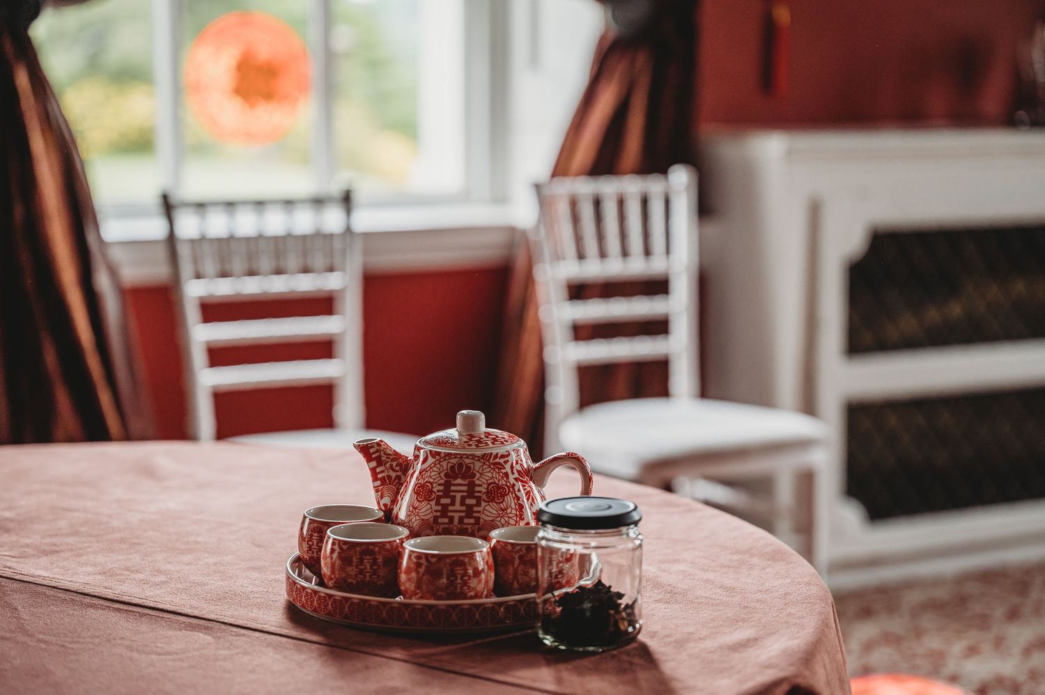 Pink teapot and teacups sit on a wooden table with white chairs in a cozy dining room interior.
