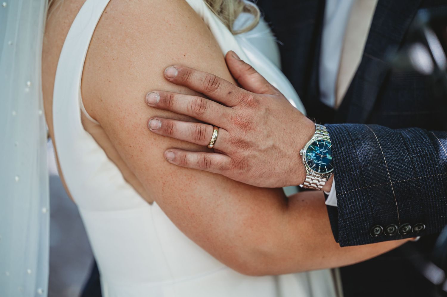 Close up shot showing a hand with wedding ring and watch against white formal attire.