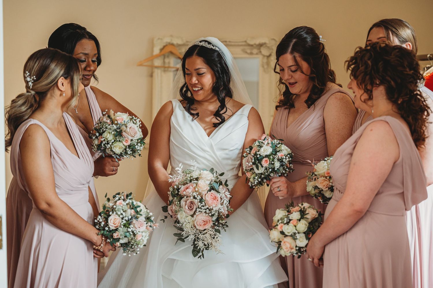 Bridesmaids in soft pink dresses share a joyful moment during a wedding celebration while holding white bouquets.