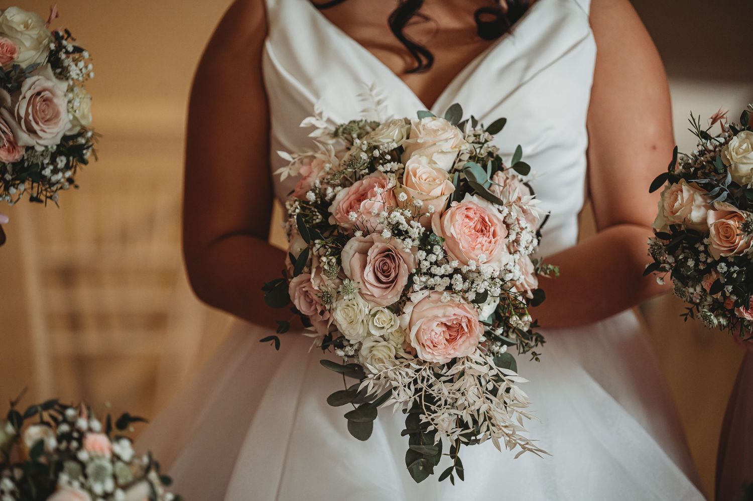 Close-up of romantic pink and white wedding bouquet with roses, eucalyptus and delicate florals against white bridal gown.