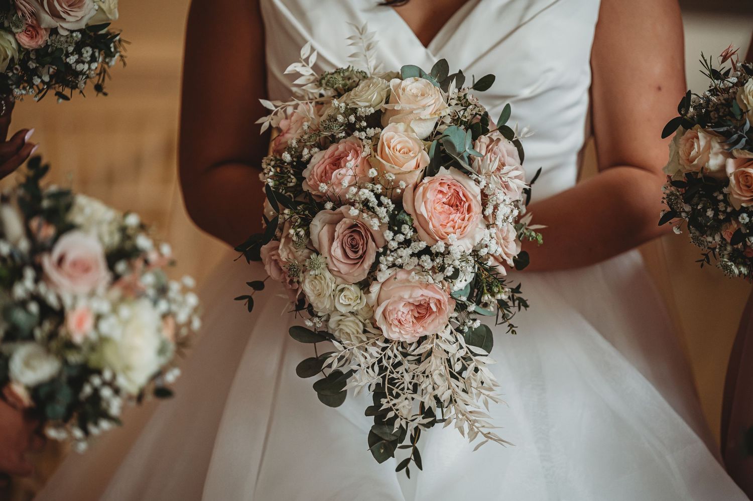 A romantic cascading bridal bouquet with blush pink roses and white flowers against a white wedding dress.