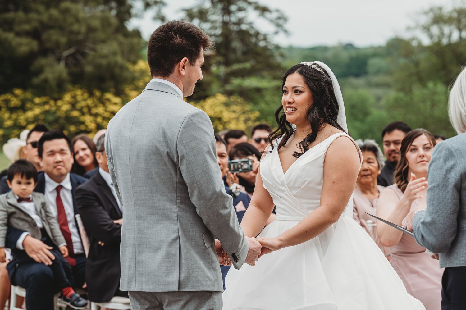 Happy couple exchanging vows during outdoor wedding ceremony surrounded by guests on a beautiful spring day.