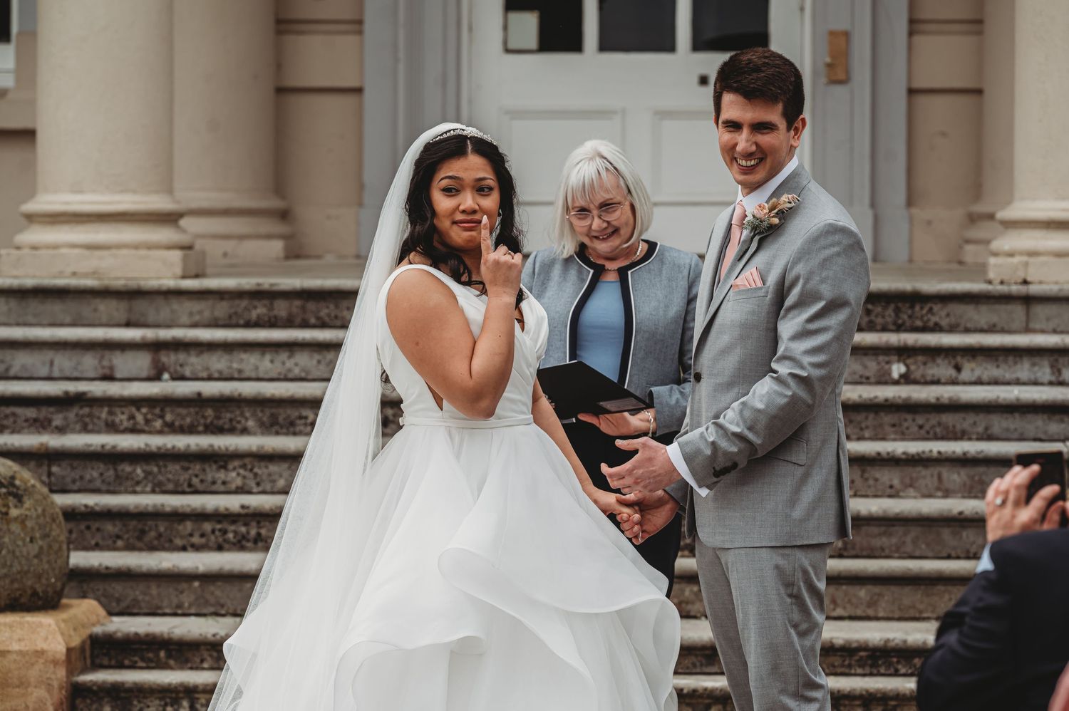 A wedding ceremony takes place on stone steps with a couple and officiant standing together in an emotional moment.