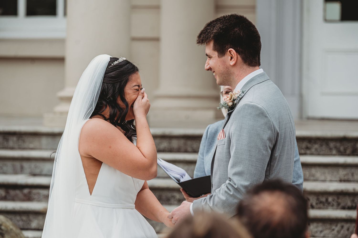 An emotional moment between a bride in a white gown and groom in grey suit during their wedding ceremony.