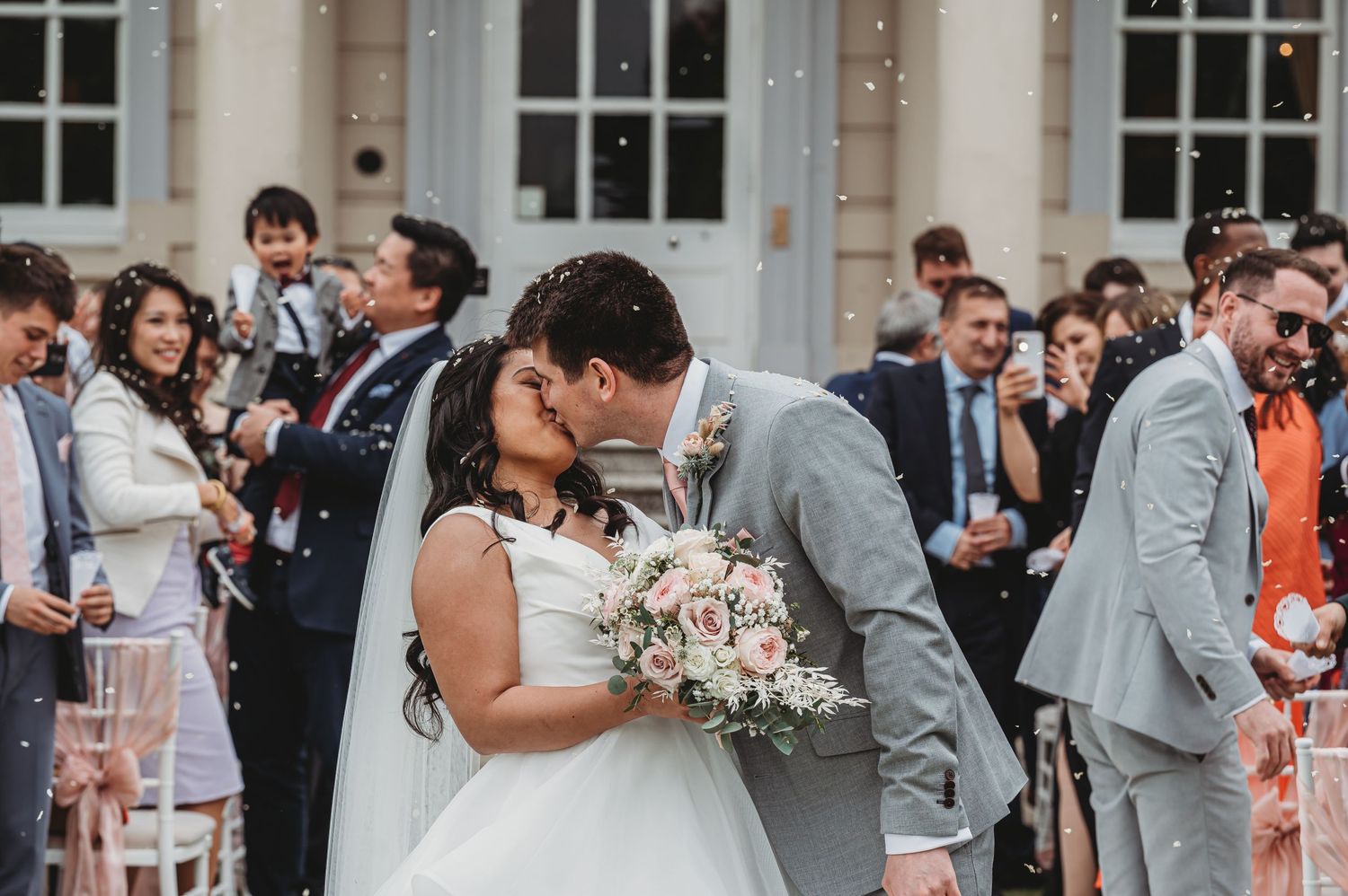 A couple shares a romantic kiss at their outdoor wedding ceremony while guests look on.