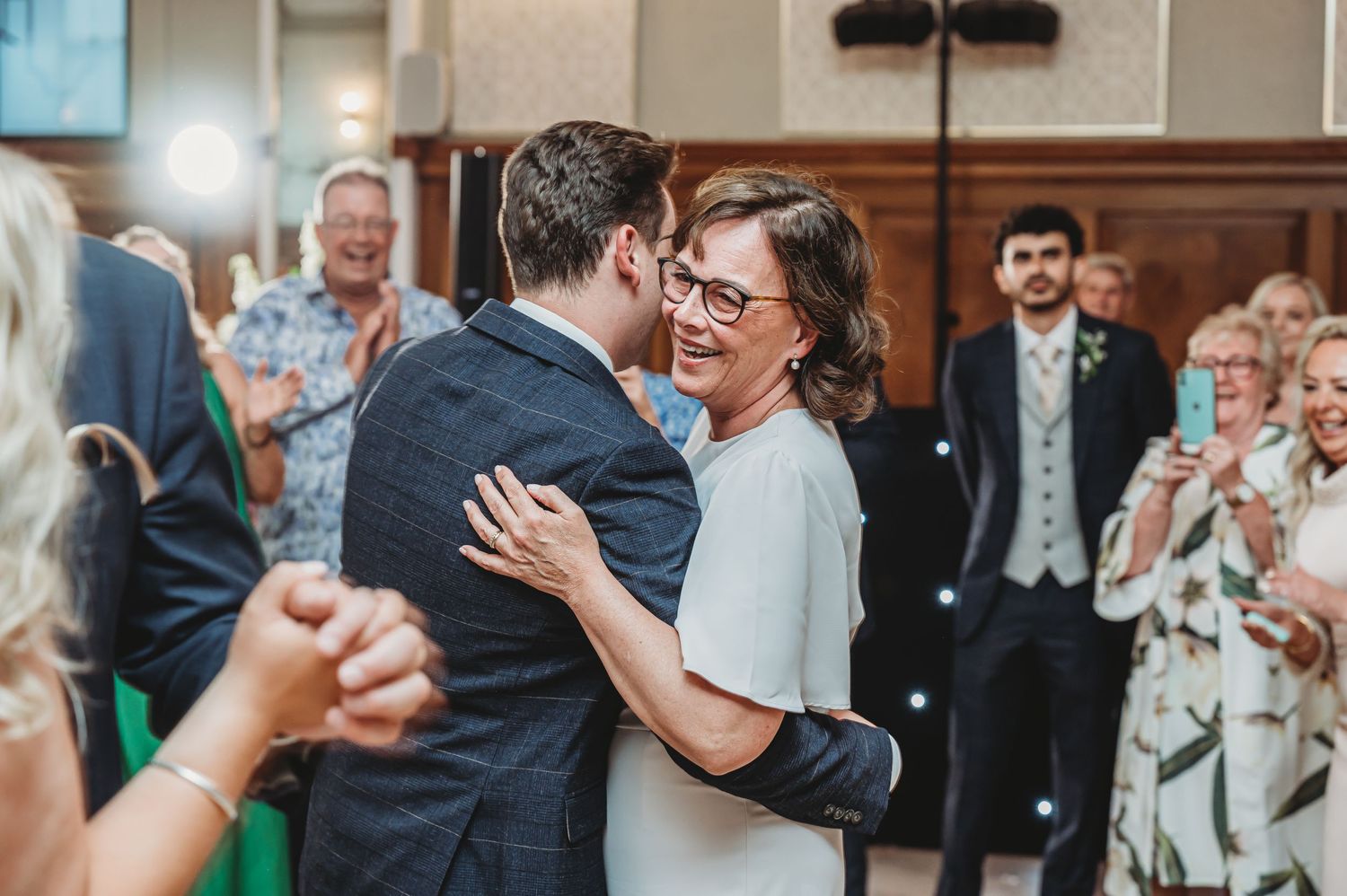 Couple sharing their first dance at wedding reception while guests watch and applaud in background.