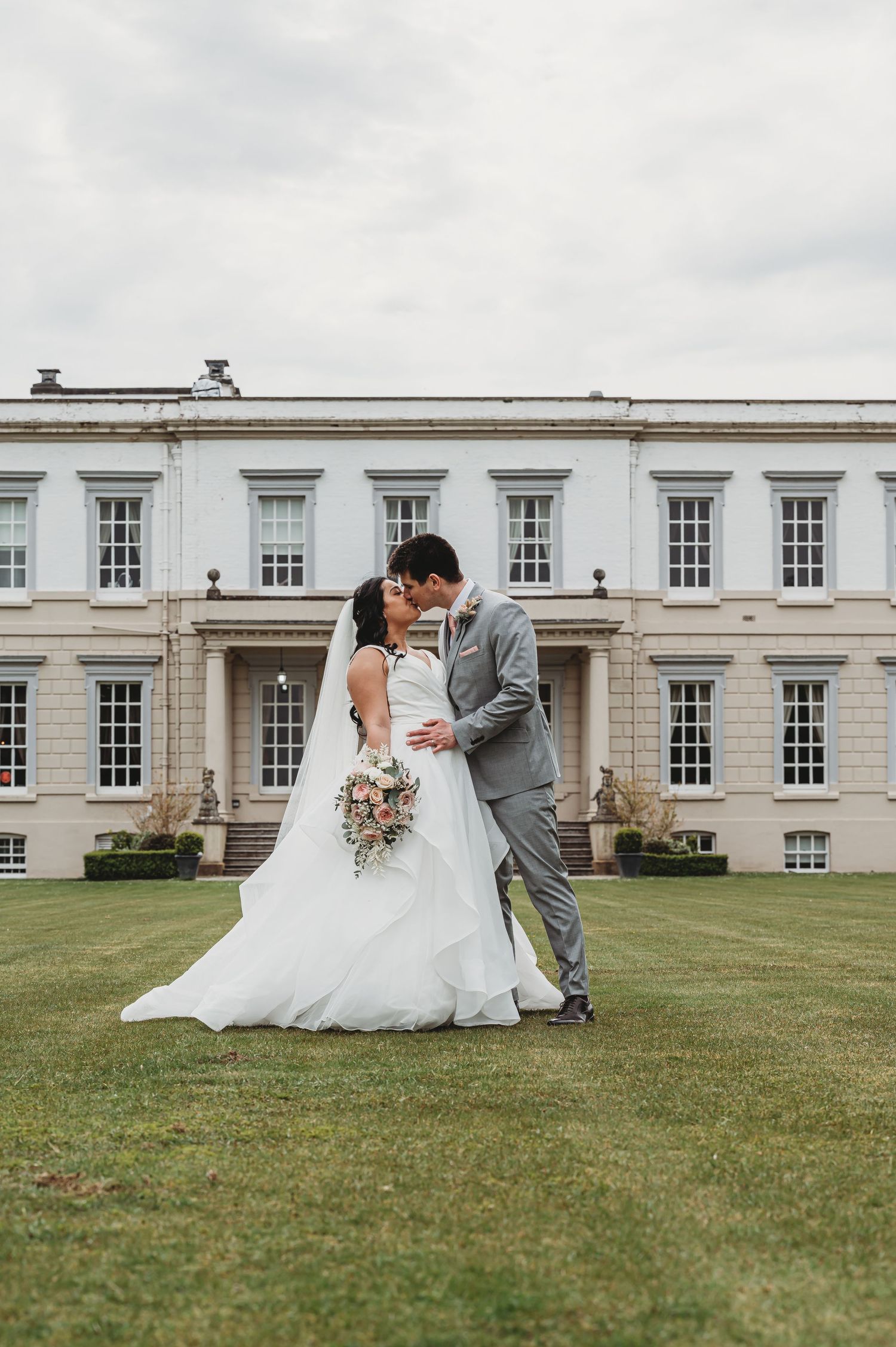 A couple sharing a romantic moment on the lawn of an elegant white Georgian mansion on their wedding day.