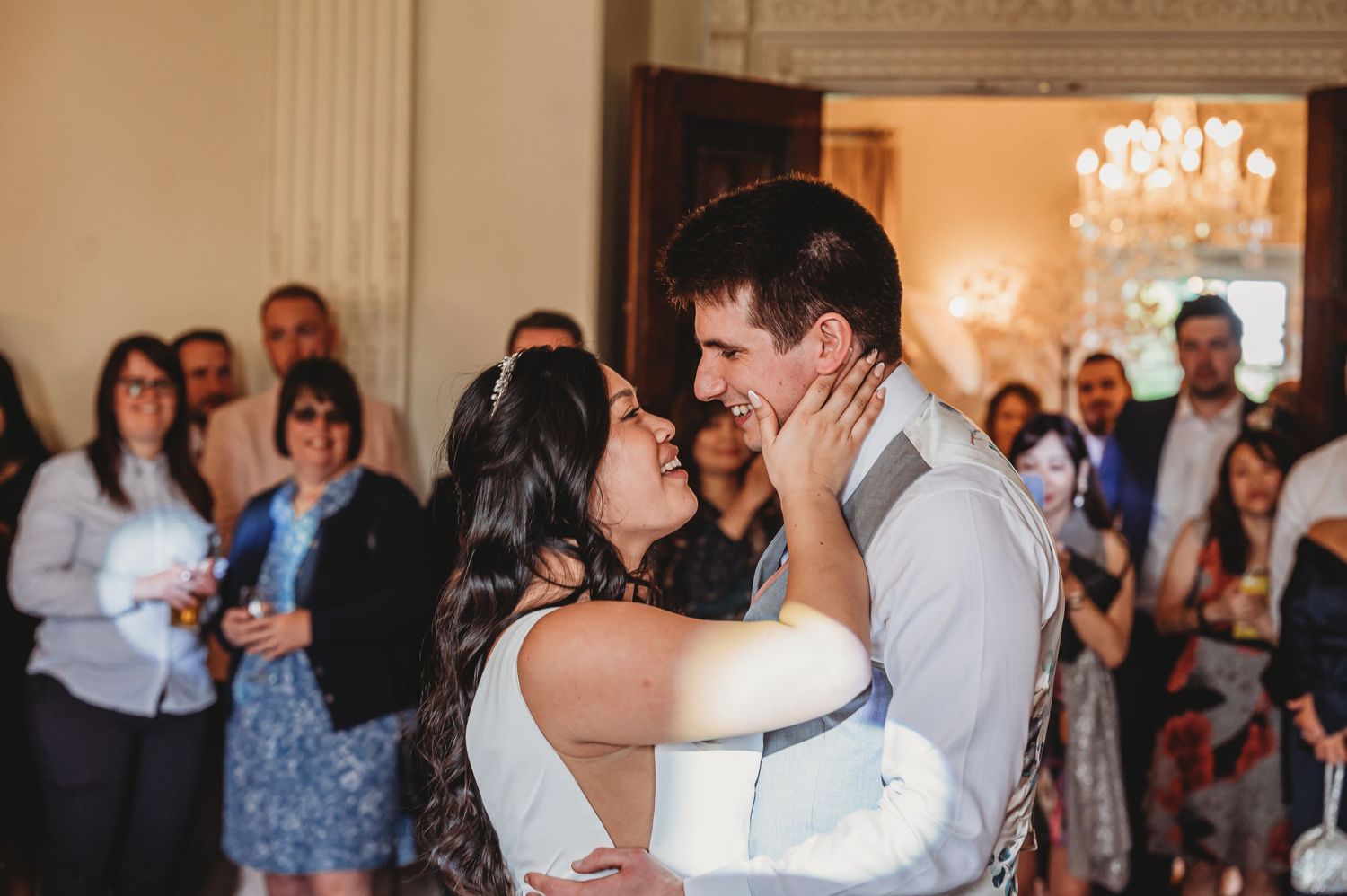 A couple shares a romantic first dance at their wedding reception in an elegant ballroom with a crystal chandelier.