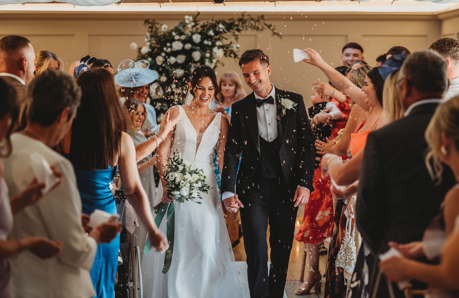 Newlyweds walking through shower of confetti with celebrating guests.