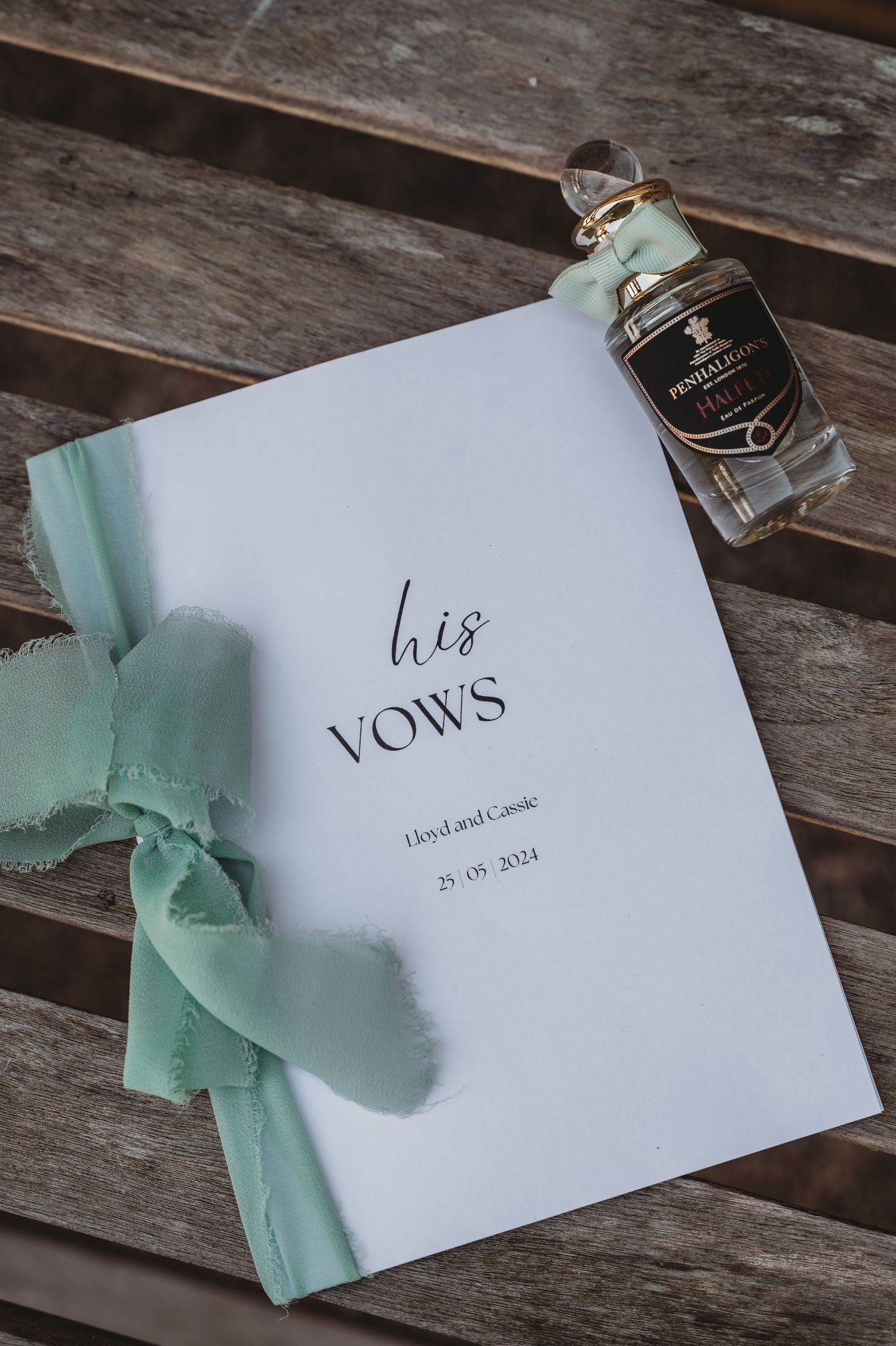 Wedding vows booklet with mint green ribbon and small bottle on wooden surface.