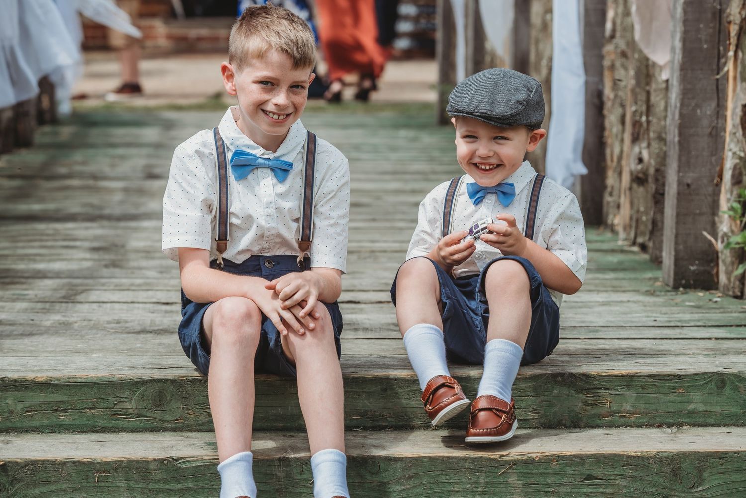 Two young children in vintage-inspired outfits with bow ties and suspenders sit together on wooden steps.
