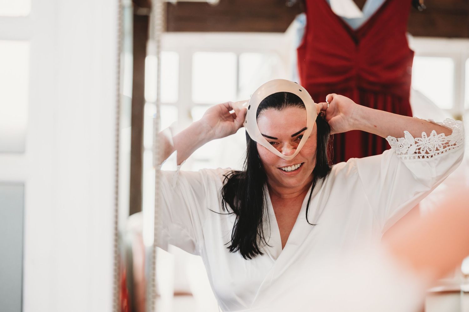 A bride in a white robe adjusts her hair while getting ready on her wedding day.