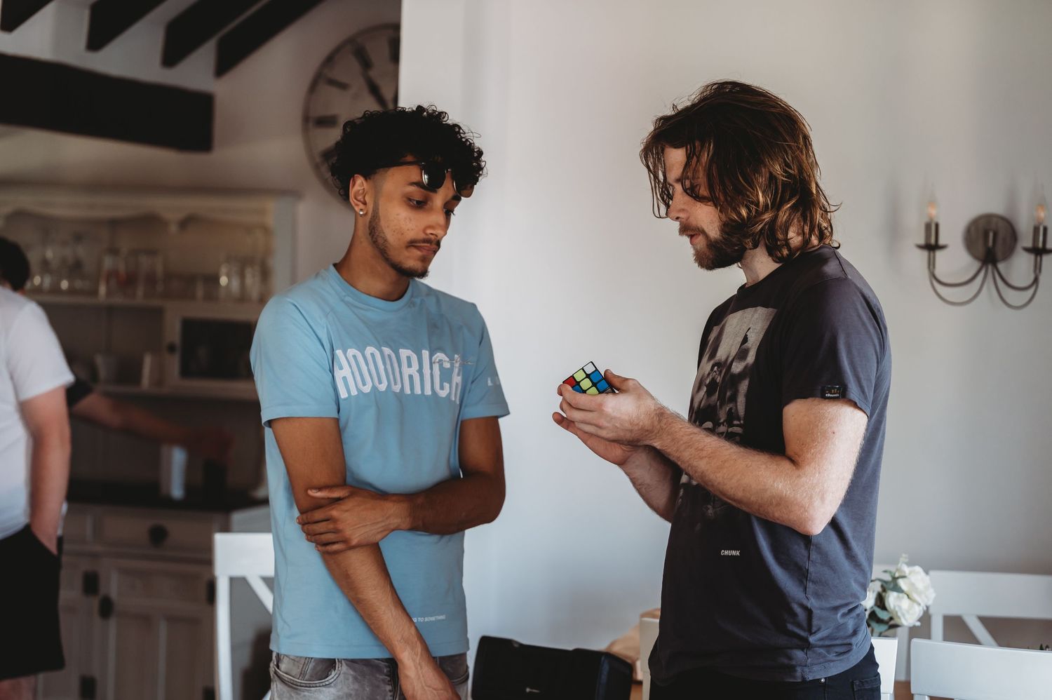 Two people stand having a conversation in a bright indoor space, one wearing a light blue shirt and one in dark clothing.