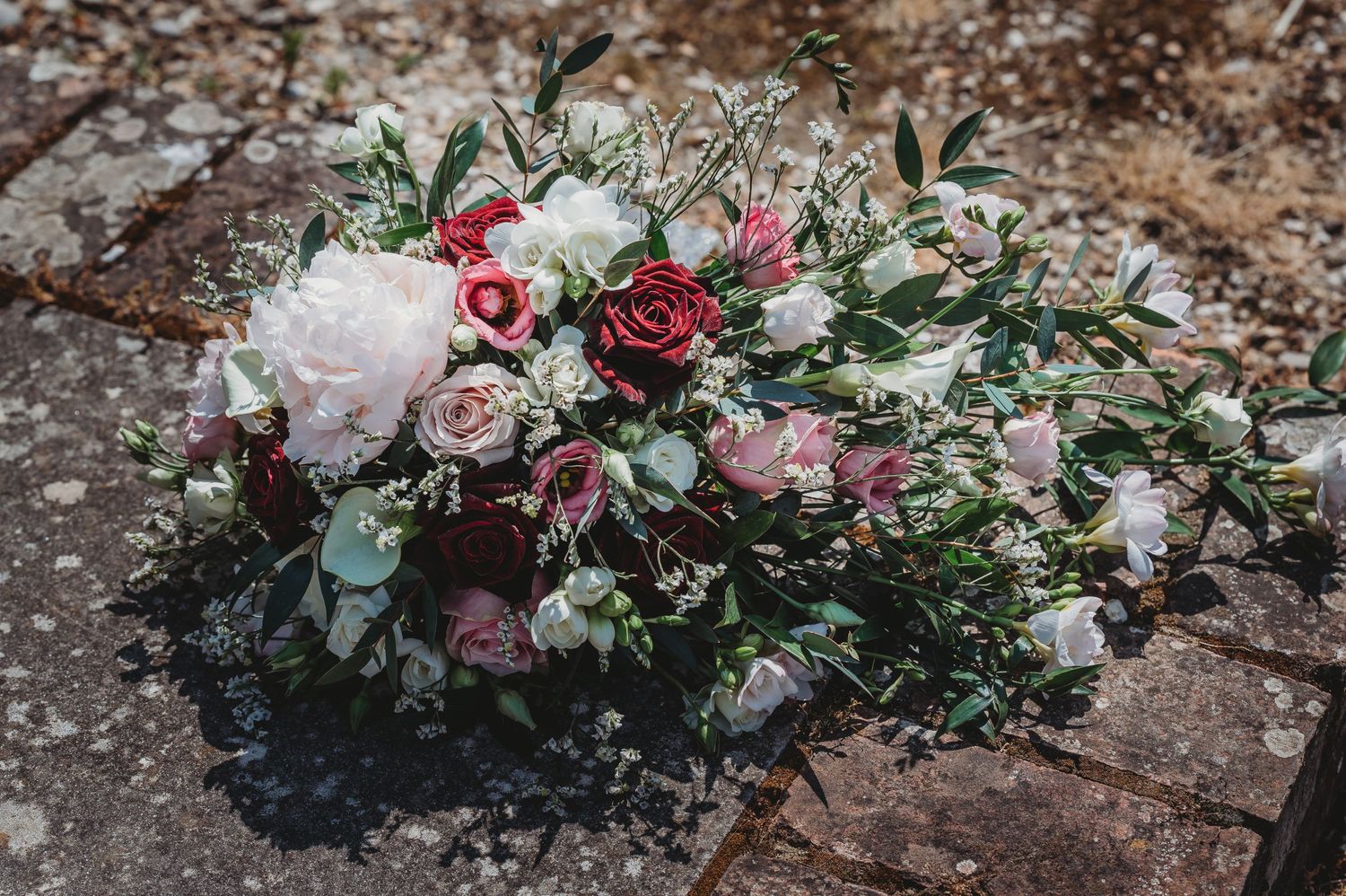 Romantic floral arrangement of pink and white roses with eucalyptus leaves resting on textured stone surface.