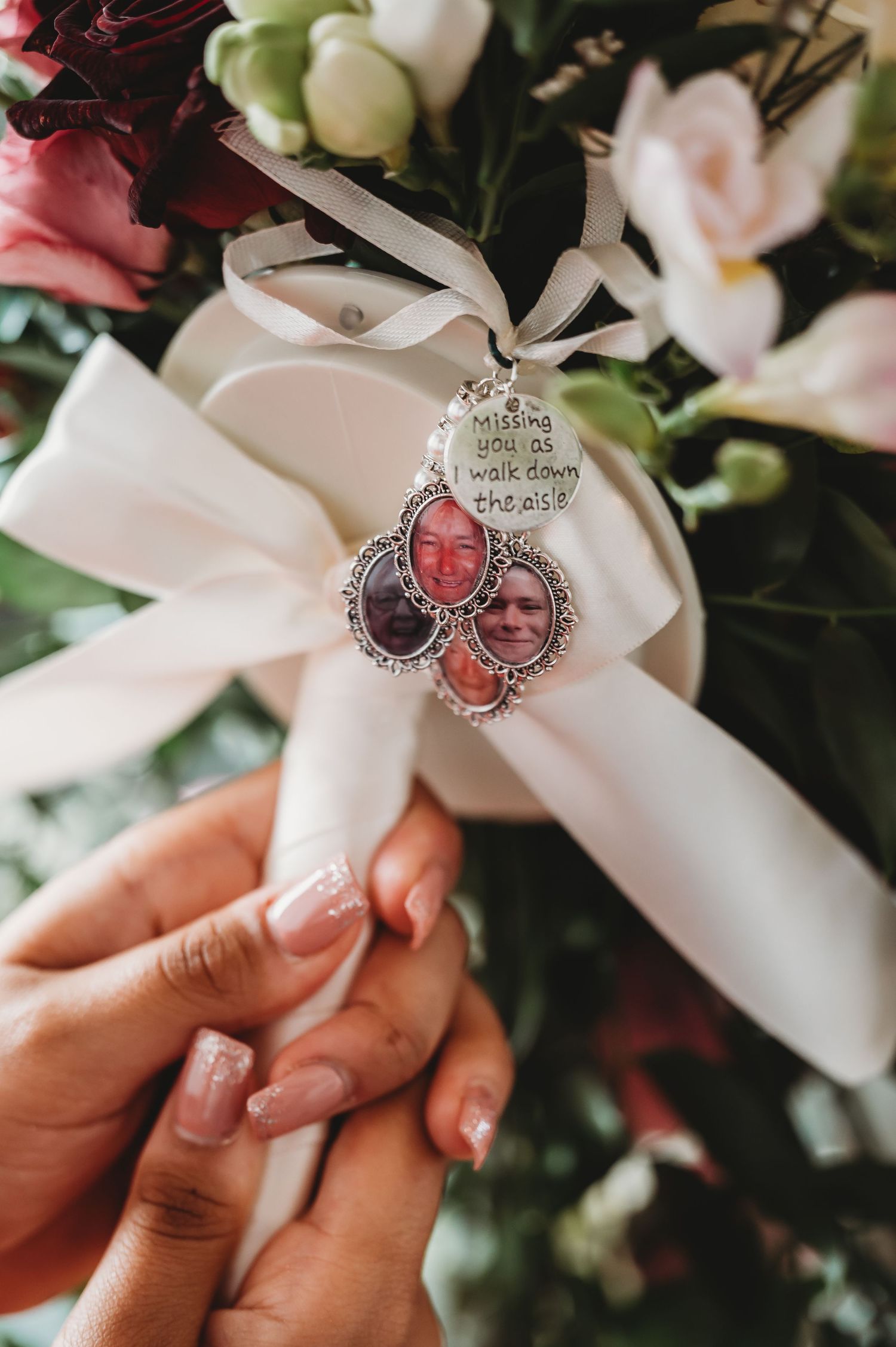 Wedding bouquet wrapped in white ribbon with a memorial photo charm pendant attachment displayed in someone's hands.