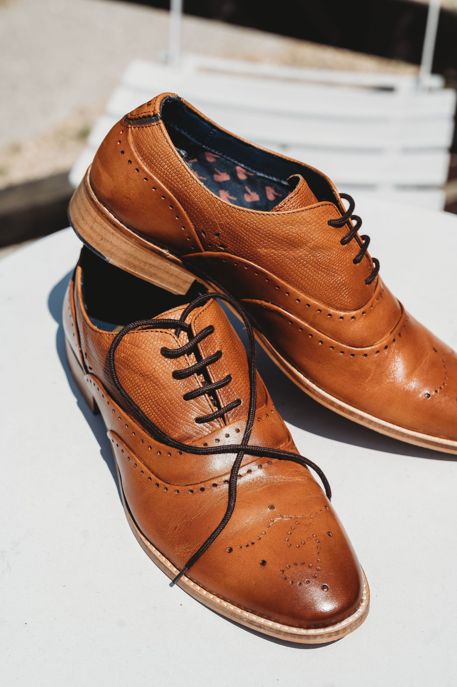 A pair of classic tan leather oxford dress shoes with brogue detailing on wooden surface in natural light.